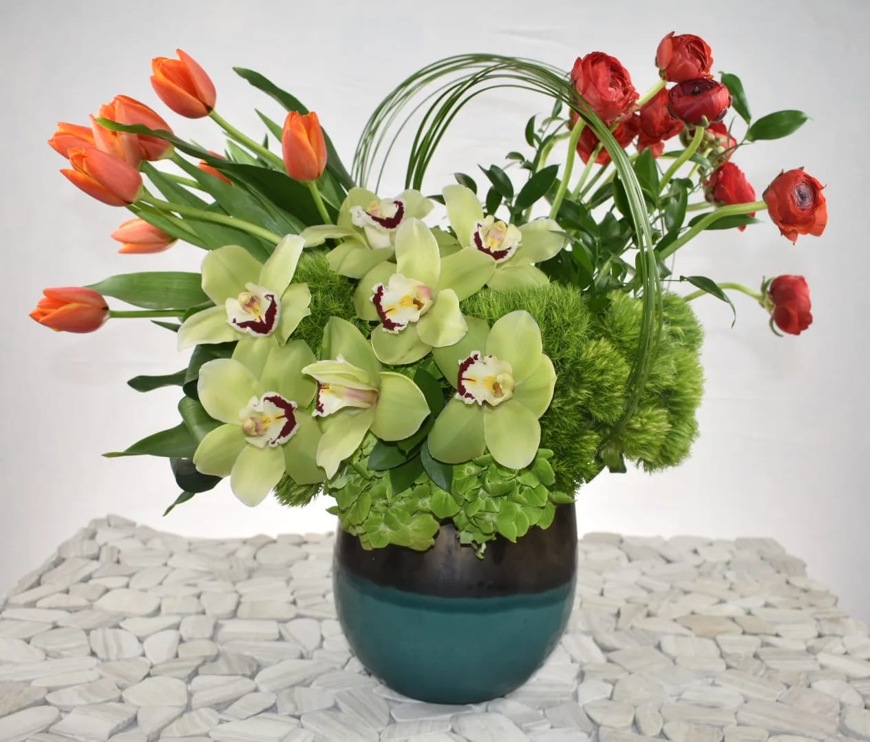  spectaculaire - This Wonderful Design Created by Sebastian the owner and head designer of Sebas Flowers. Was created in a beautiful ceramic vase with a gold and blueish color, orange tulips on one side red Ranunculus on the other side perfectly combined with, some green leafs folded up nicely  green Dianthus, green hydrangeas and green cymbidium and to finish up the elegant look some bear grass going across. Perfect for any occasion   Perfect for  birthday flowers anniversary flower  just because flowers  congratulations flowers  Get well flowers  Christmas flowers Valentines Day flowers Mother's Day flowers  