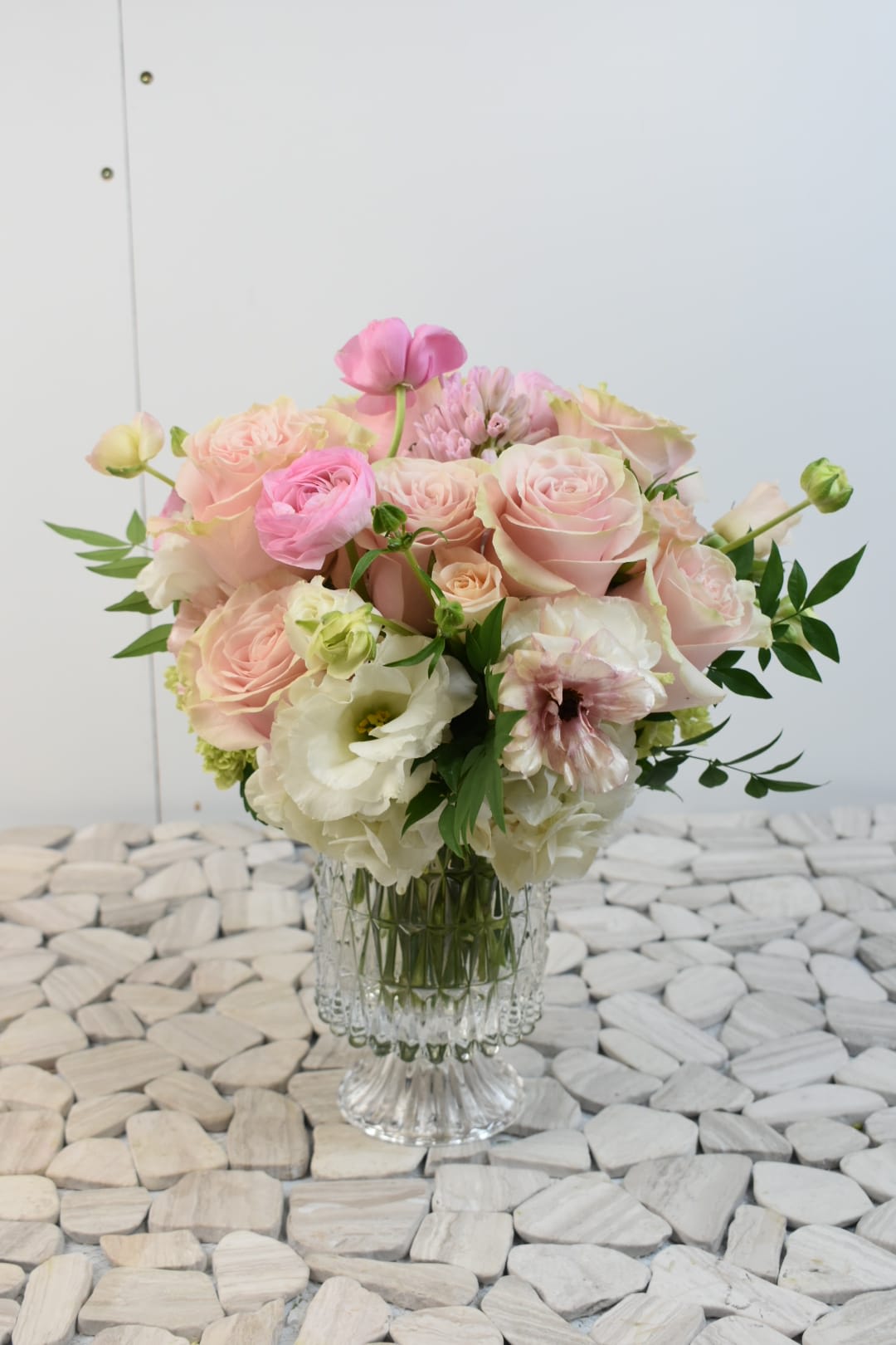 Round arrangement of pale pink and white roses and other blooms in a clear glass vase