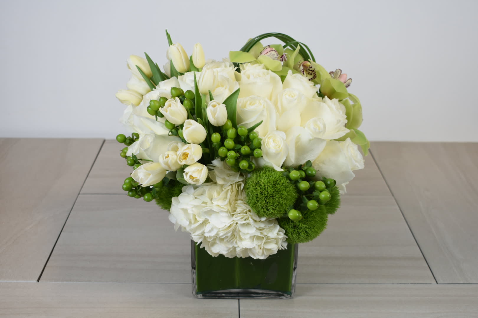 White floral arrangement in a green glass vase with green accents