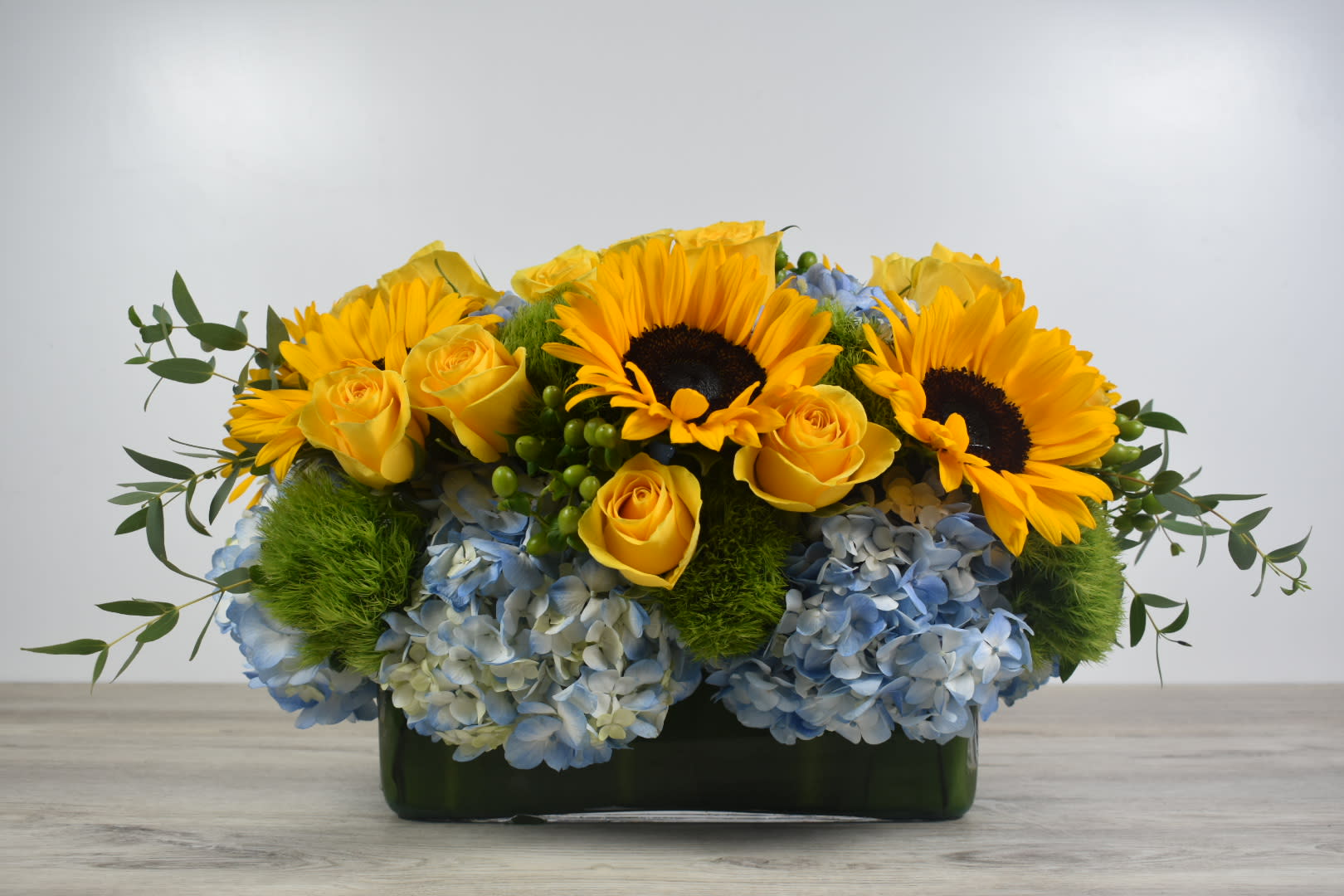 Sunflower elegance - This Sunflower elegance design comes in a glass rectangular vase  With a nice combination of blue hydrangeas, yellow roses and some beautiful sunflowers with a hint of greenery to finish the look   Perfect for  birthday flowers anniversary flower  just because flowers  congratulations flowers  Get well flowers  Christmas flowers Valentines Day flowers Mother's Day flowers