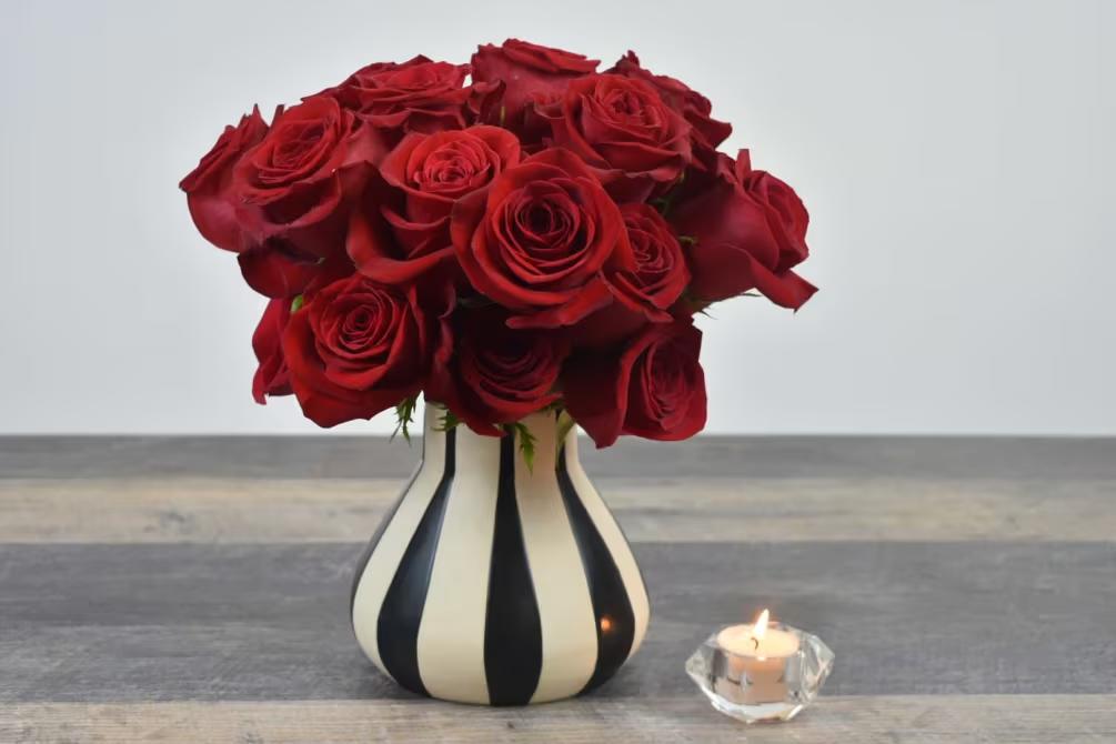 Red rose bouquet in a striped vase beside a lit candle