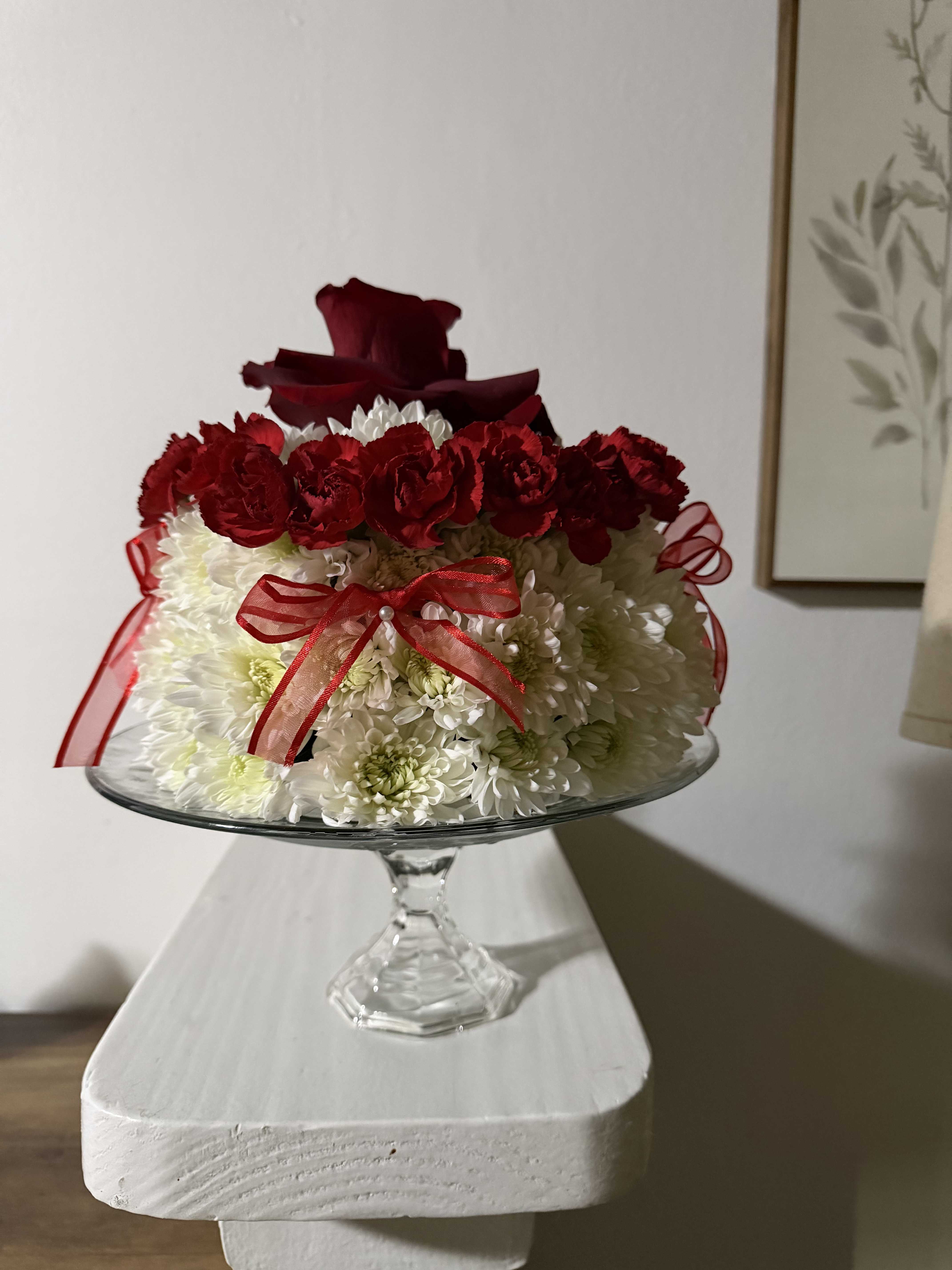 Red and white floral arrangement in a glass pedestal bowl with ribbon
