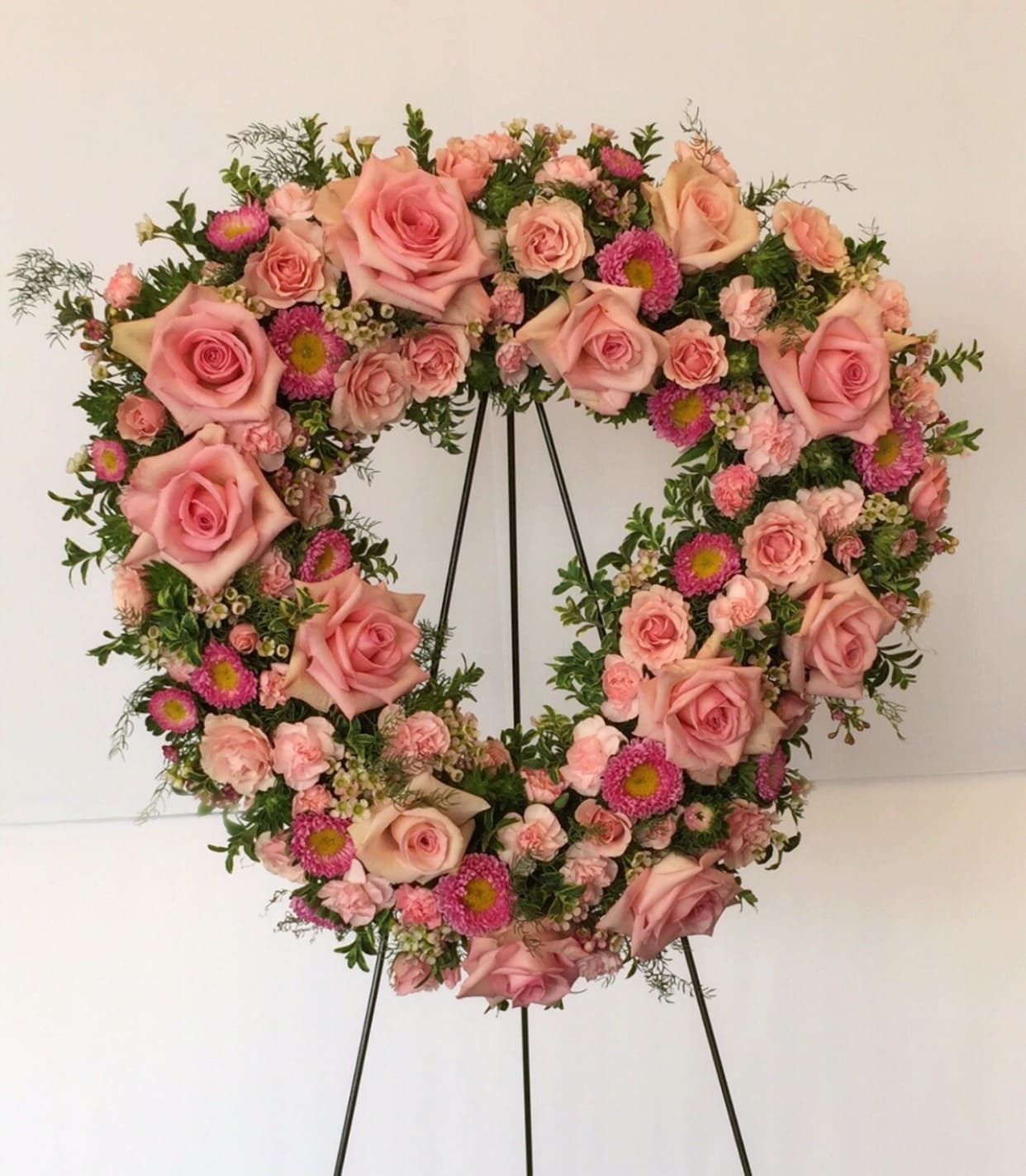 Heart-shaped floral wreath of pink roses and small pink blooms on a stand