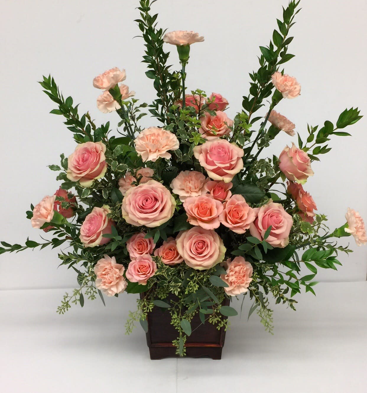 Pink roses and peach carnations arranged in a dark wooden container