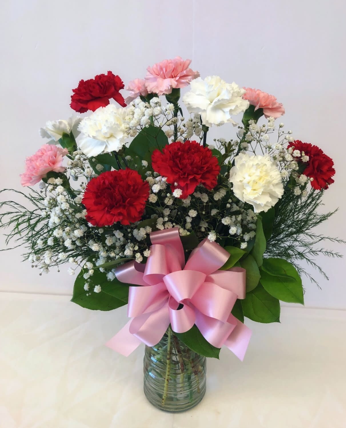 Bouquet of red, white, and pink carnations in a glass vase with a pink ribbon