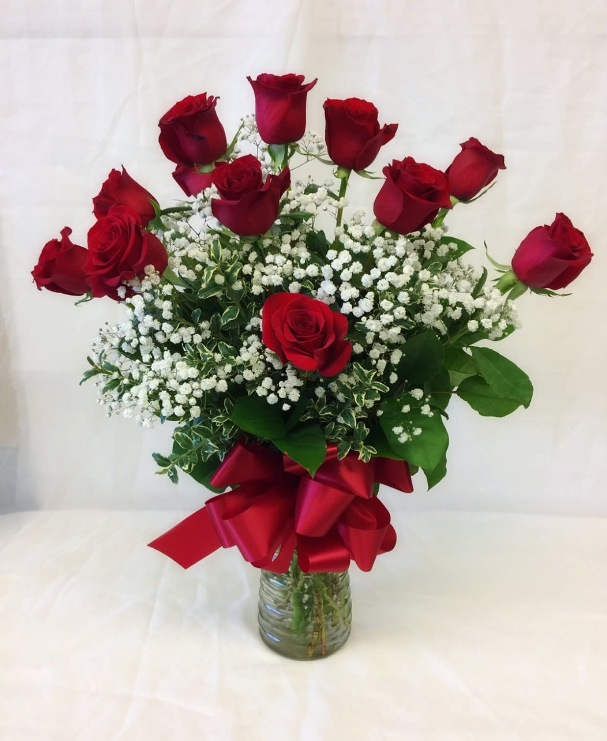 Red roses arranged in a glass vase with baby's breath and a red ribbon