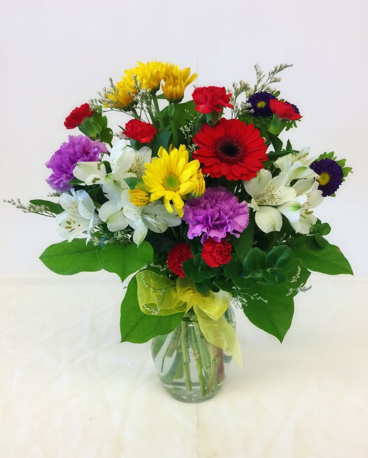 Mixed bouquet of colorful flowers in a glass vase with a yellow ribbon
