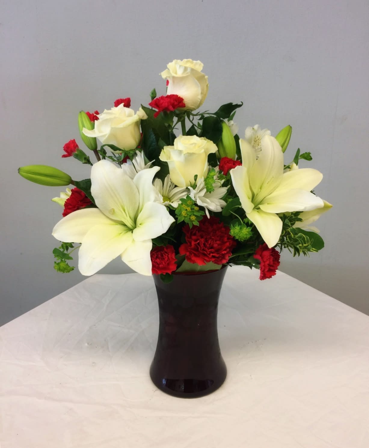 White lilies and roses with red carnations in a dark vase