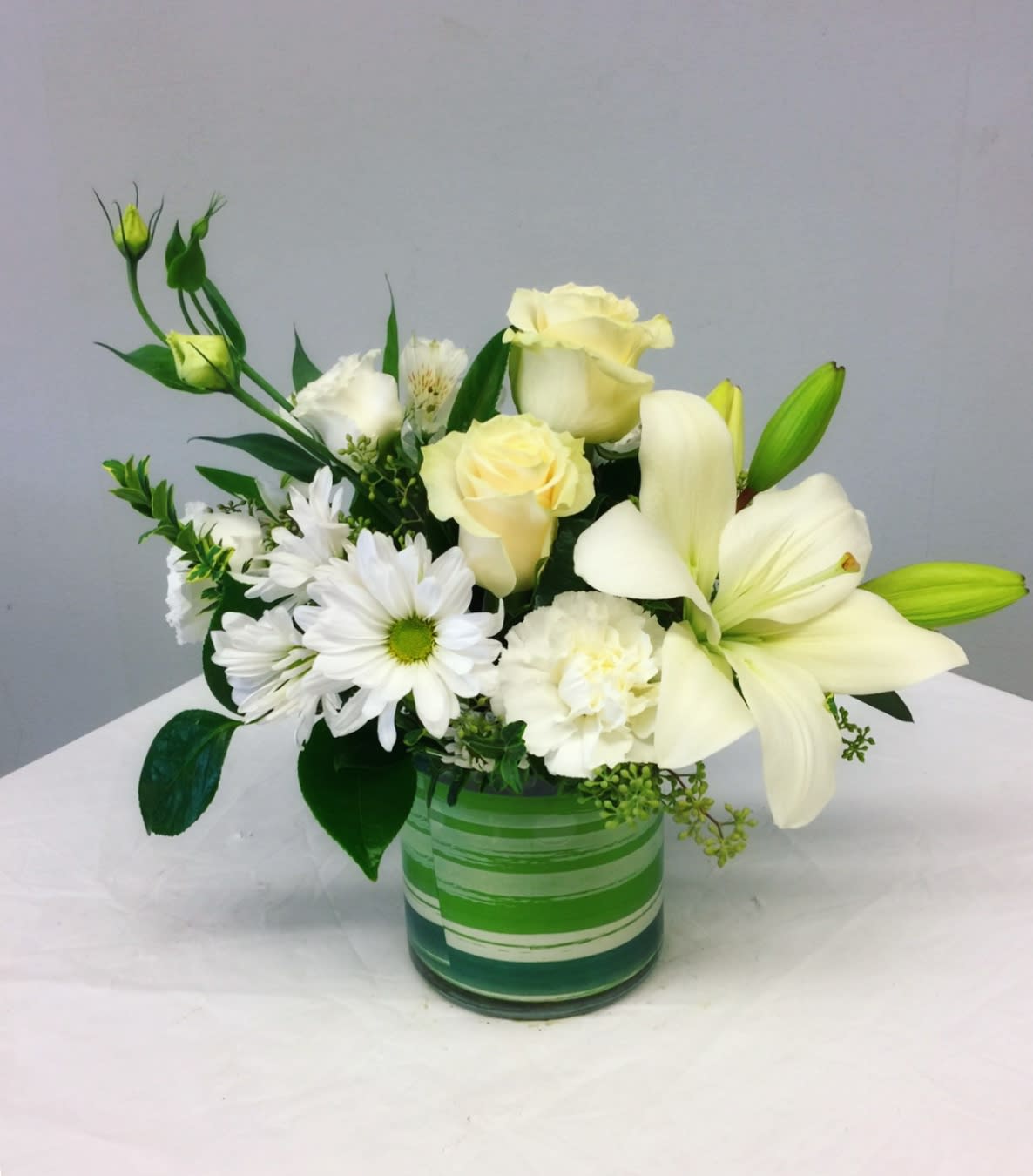 White lilies, roses, and daisies arranged in a green glass vase