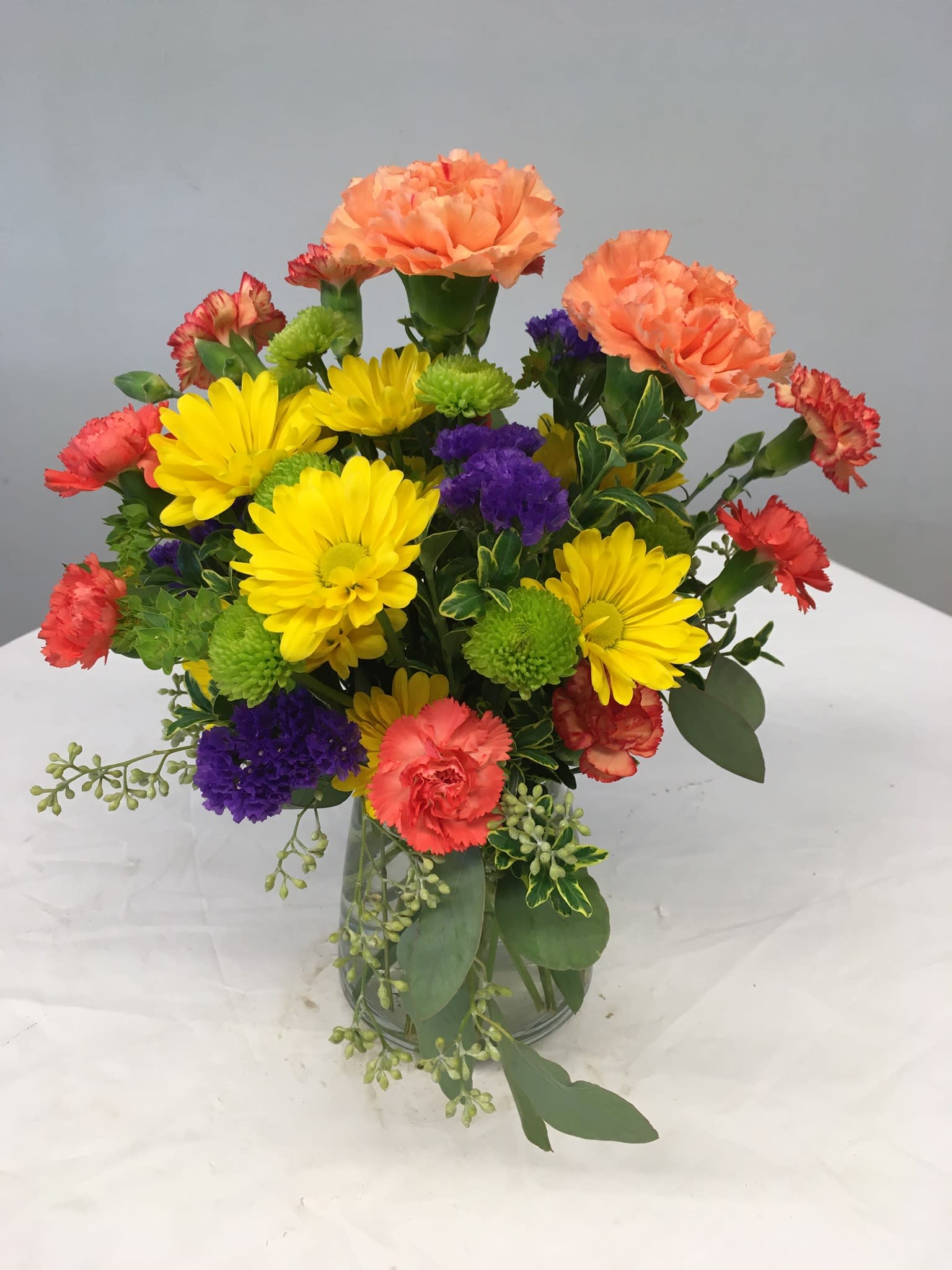 Mixed bouquet of yellow daisies, carnations, and purple blooms in a glass vase