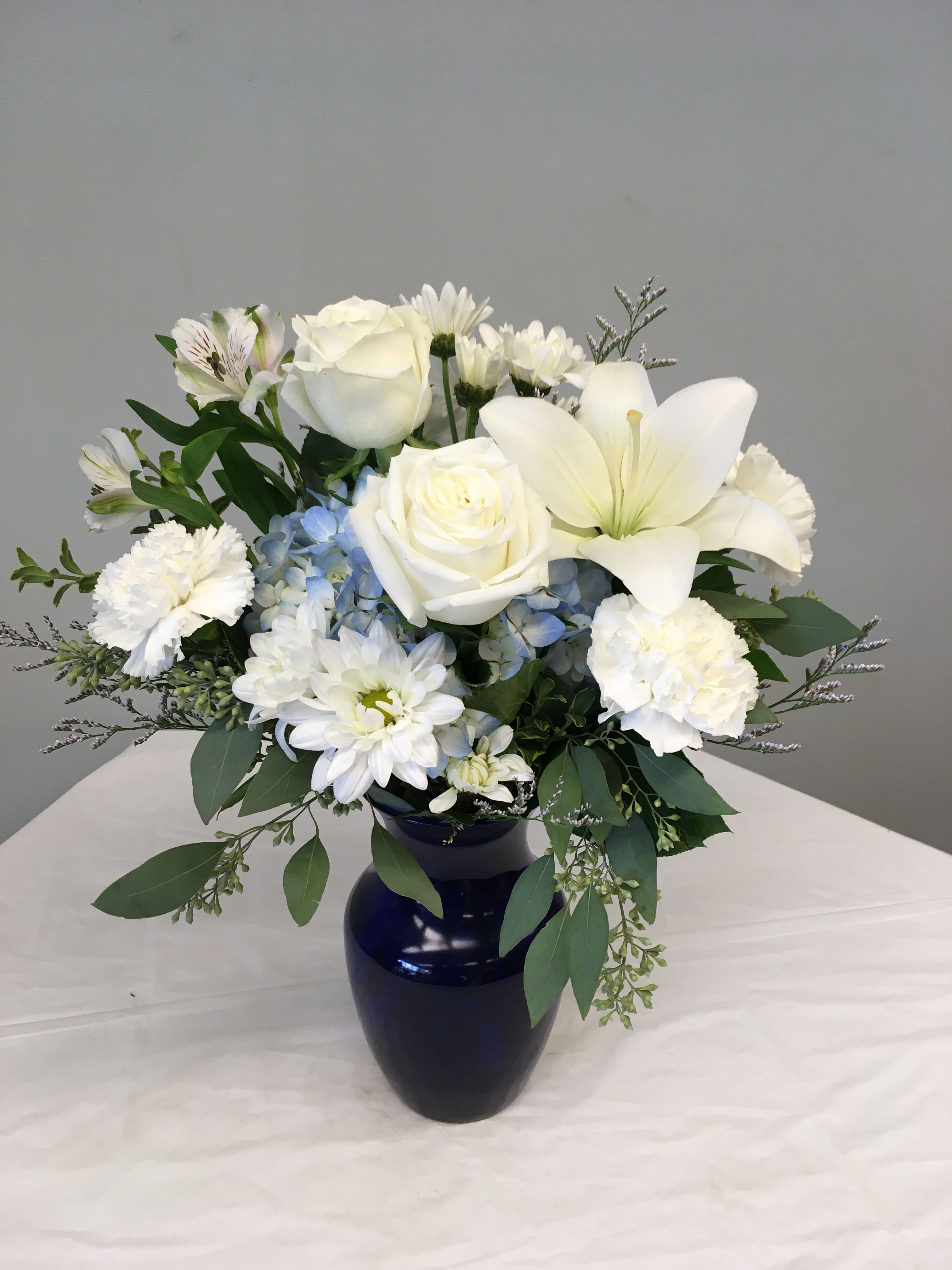 White roses, lilies, and daisies in a dark blue vase