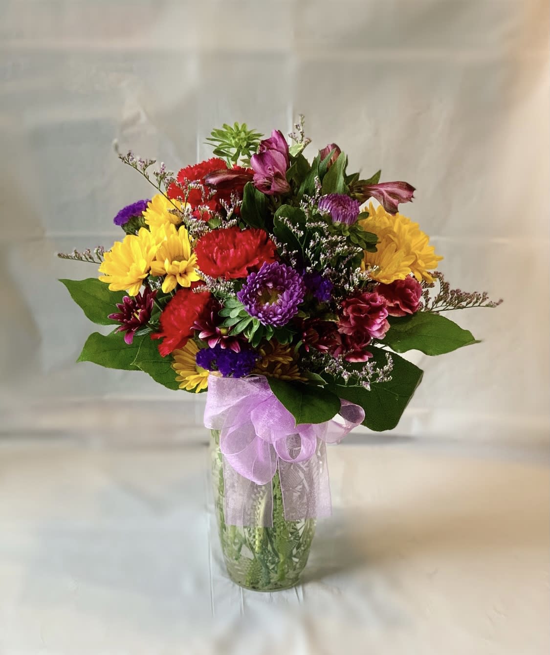 Colorful mixed bouquet in a clear glass vase with a lavender ribbon