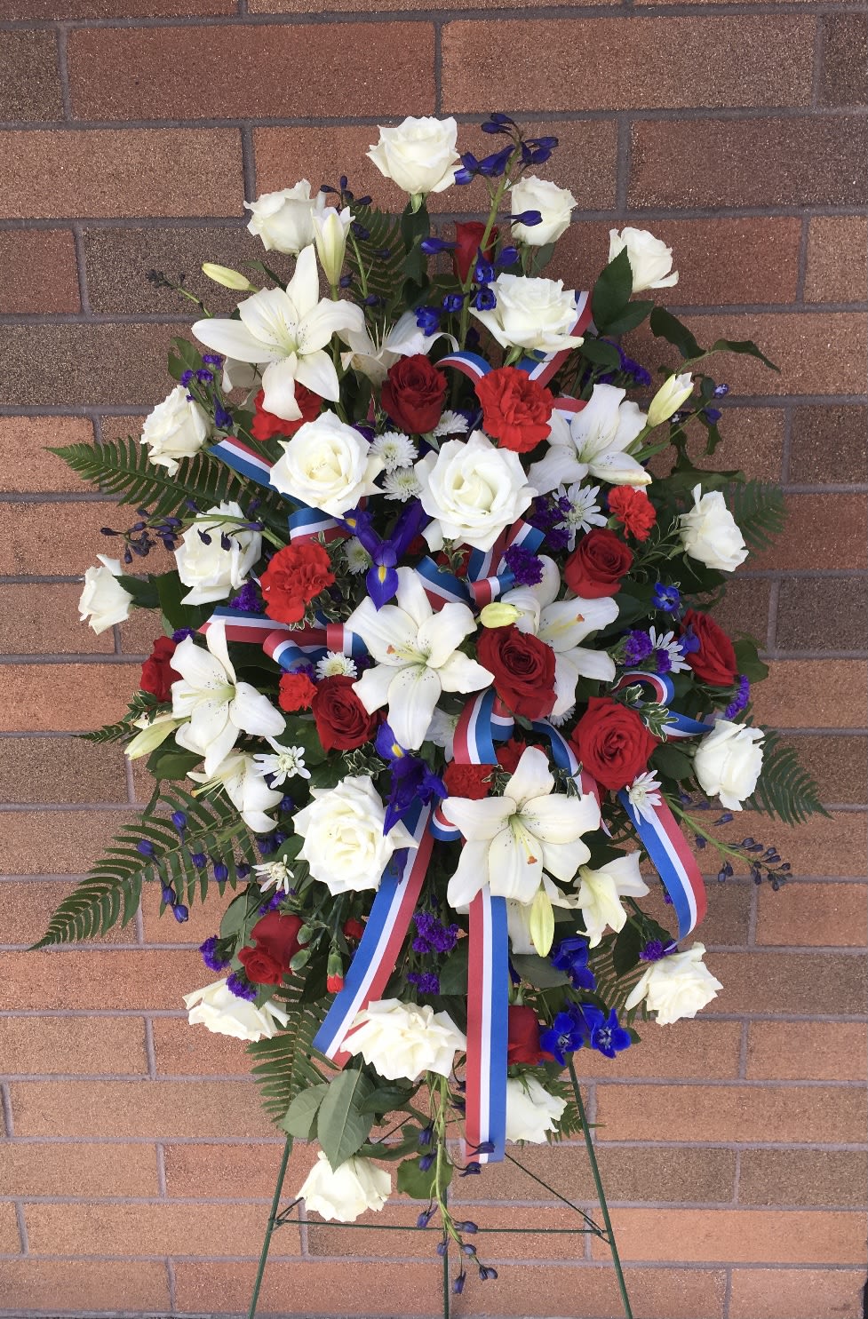 Standing floral spray with red and white roses, lilies, and ribbon streamers