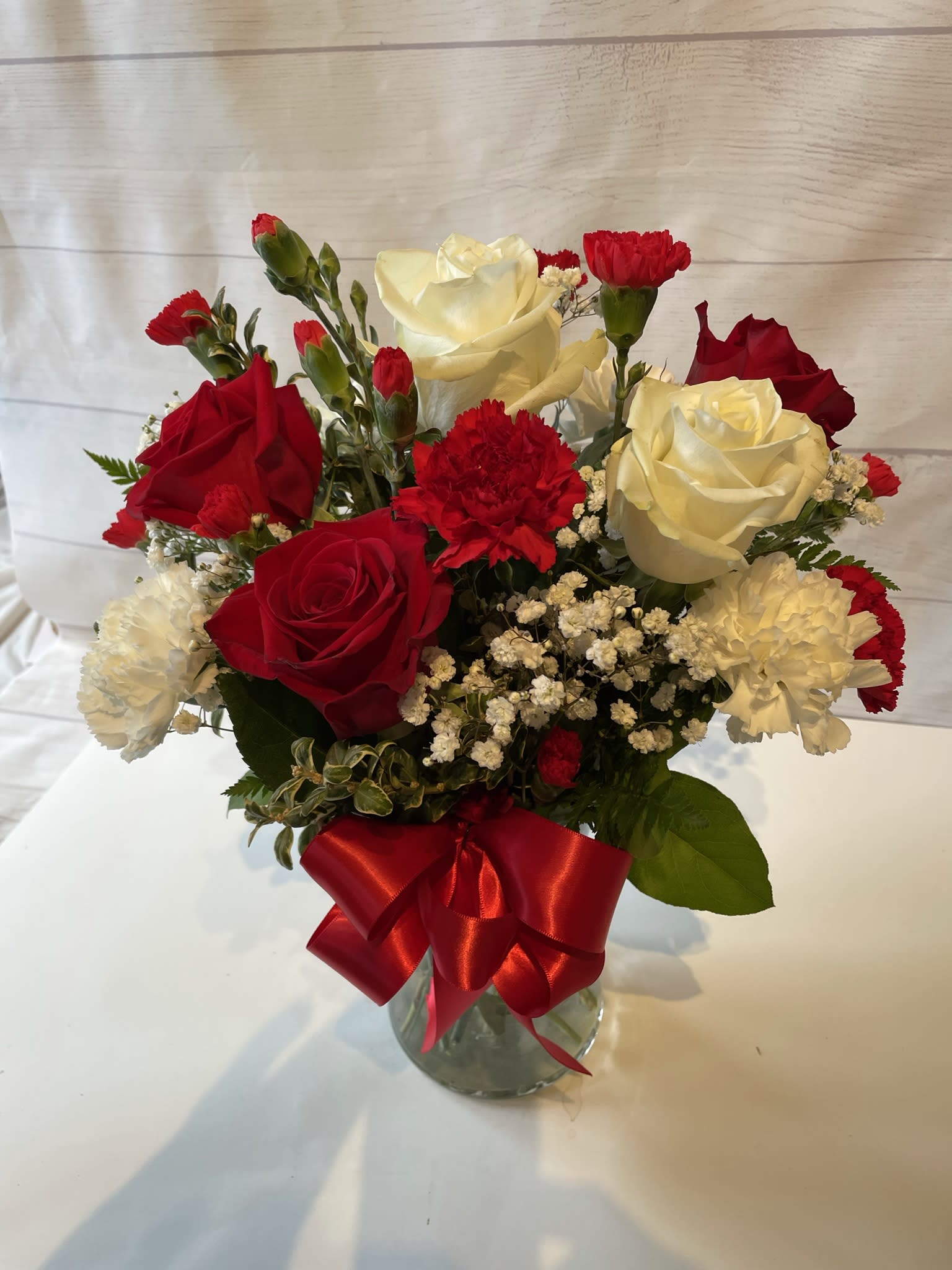 Red and white roses with carnations in a glass vase tied with a red ribbon