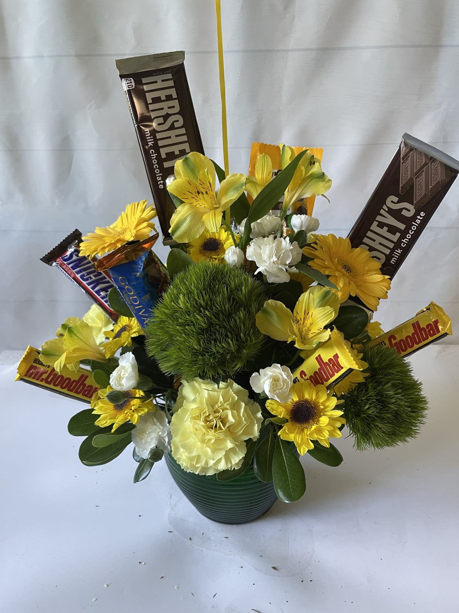 Yellow flowers and chocolate bars arranged in a green pot.