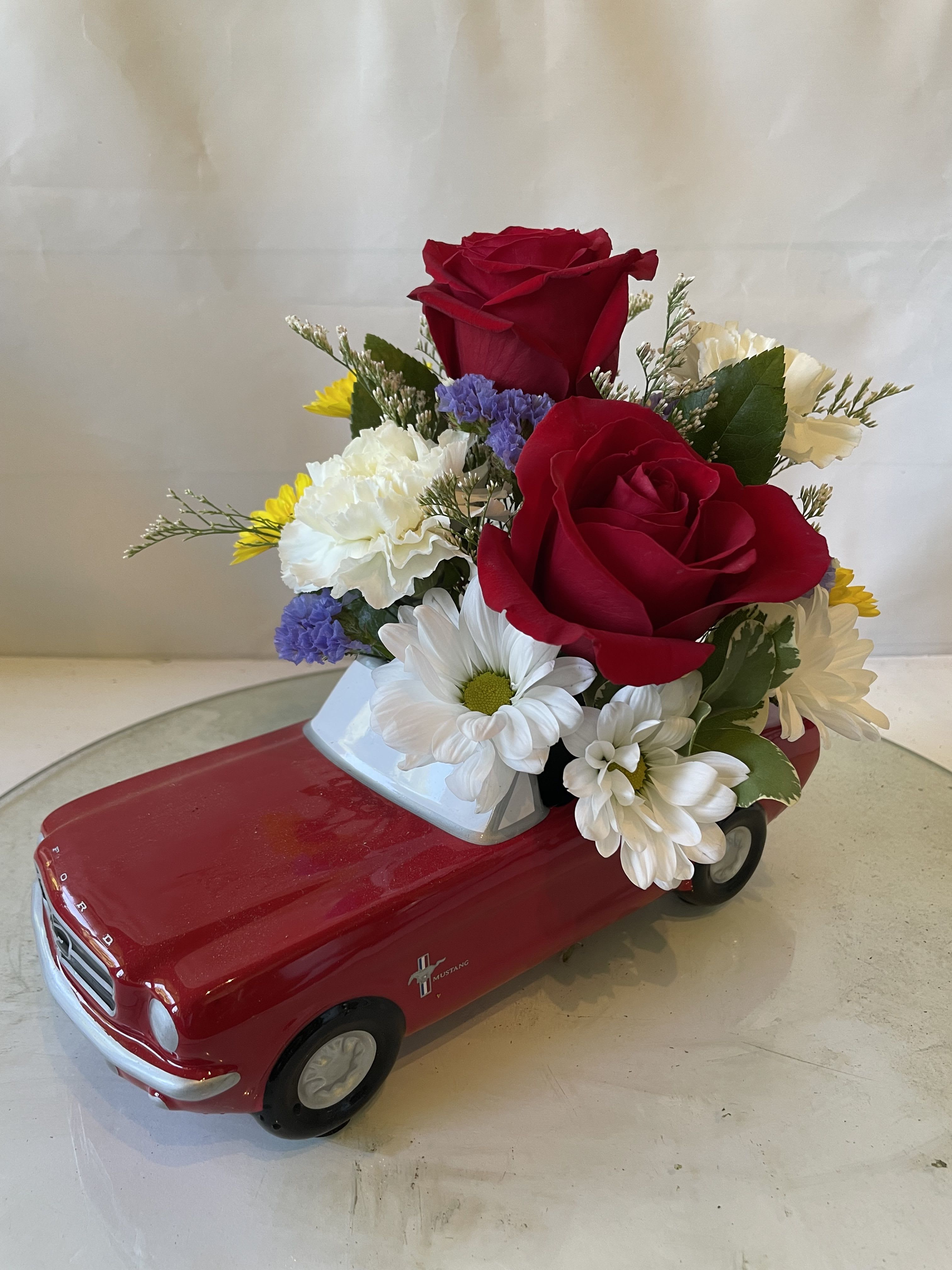 Red rose and daisy arrangement in a red toy car