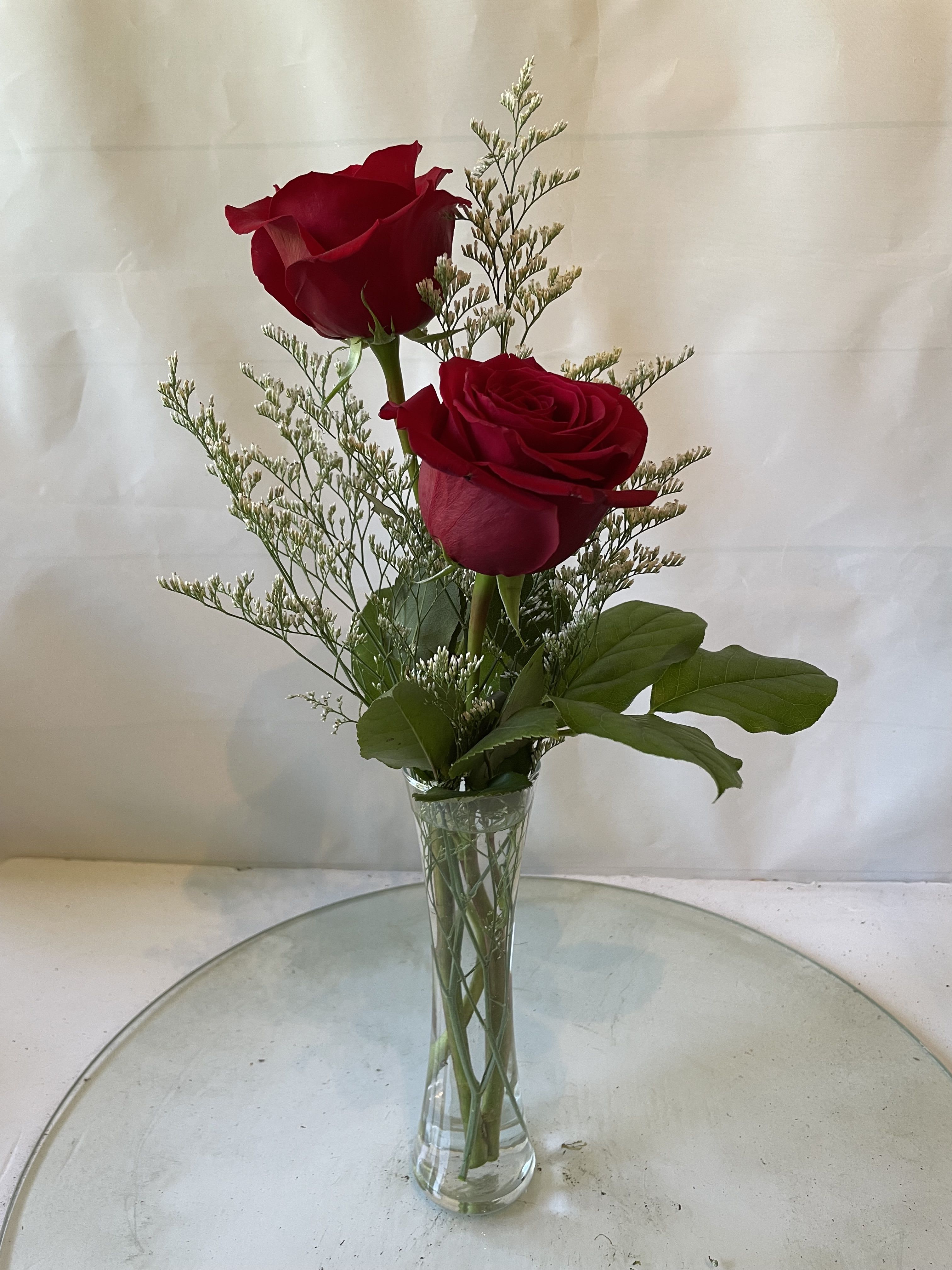 Two red roses in a clear glass vase with airy filler