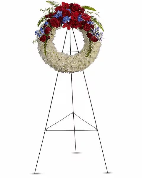 Standing floral wreath with red roses, blue flowers, and white blooms on an easel