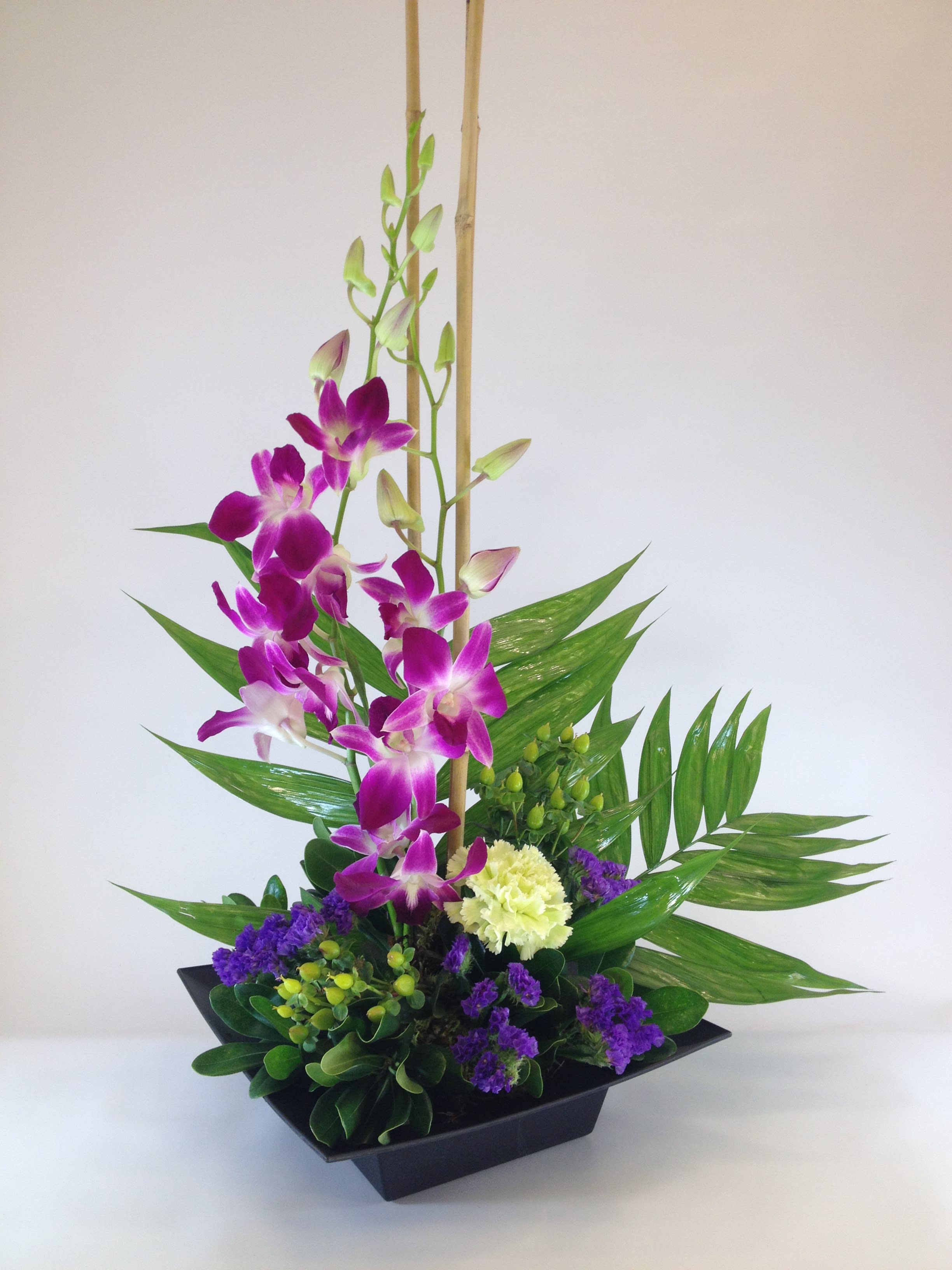 Purple orchids arranged in a black square vase with green foliage
