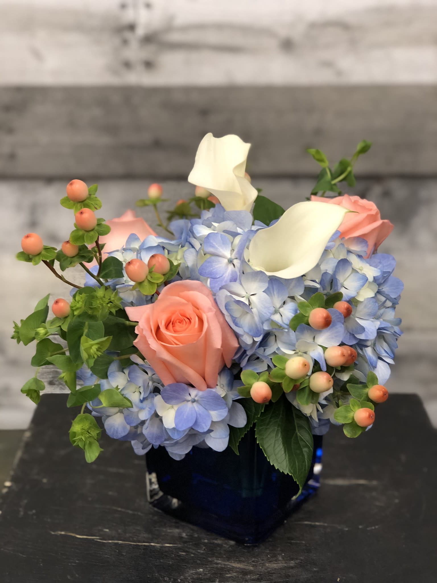 Blue hydrangeas with pink roses and white calla lilies in a dark vase