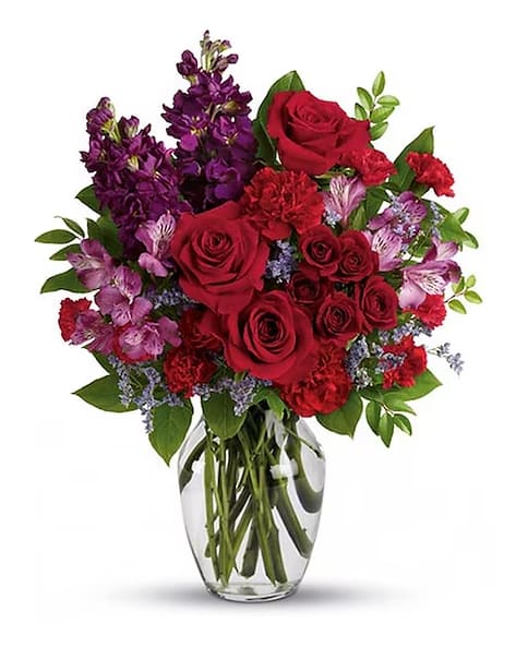 Red roses and purple flowers arranged in a clear glass vase