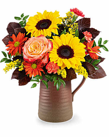 Bouquet of sunflowers, roses, and orange daisies in a brown pitcher vase