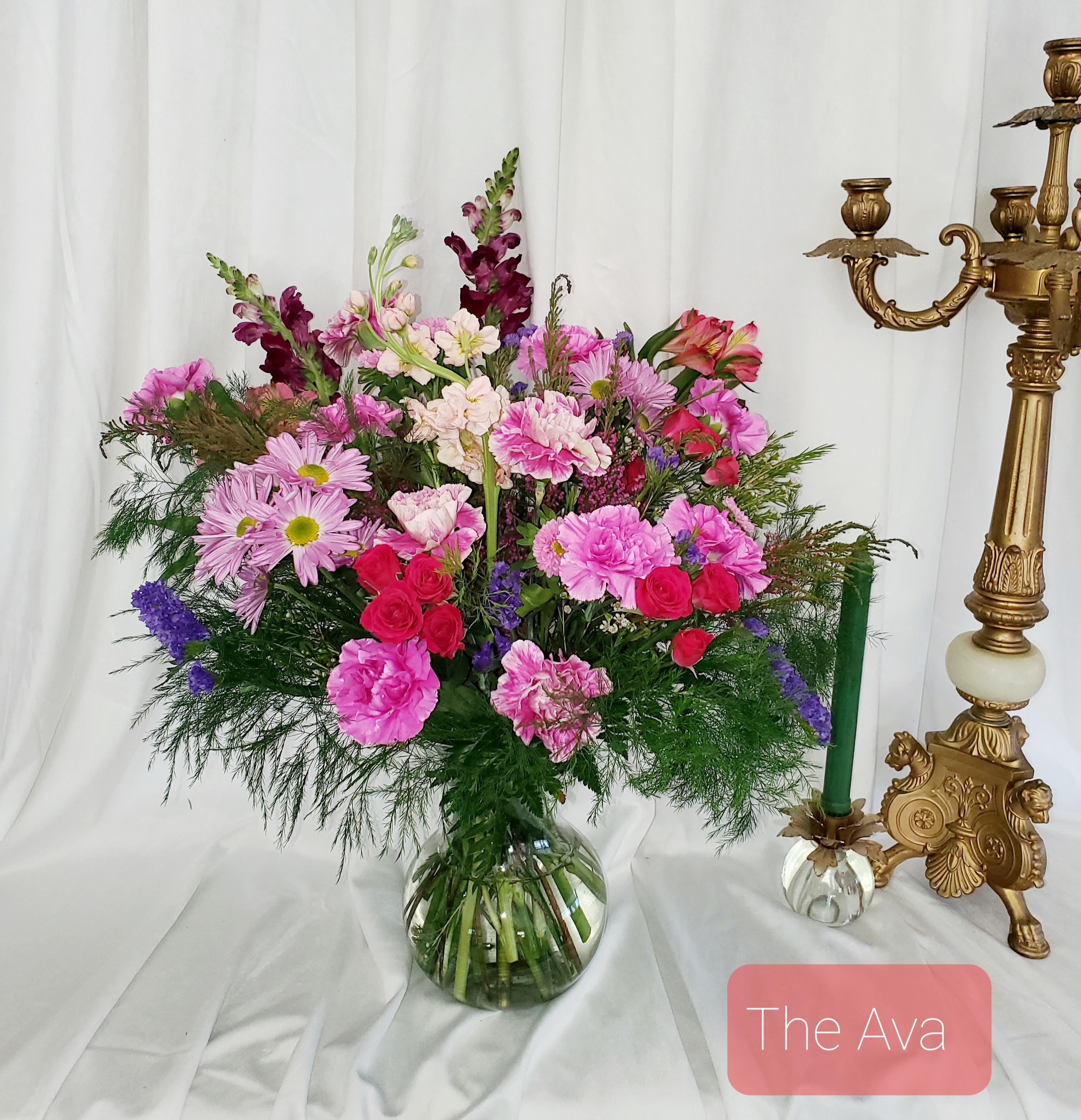 Pink and purple mixed bouquet in a glass vase beside a gold candlestick