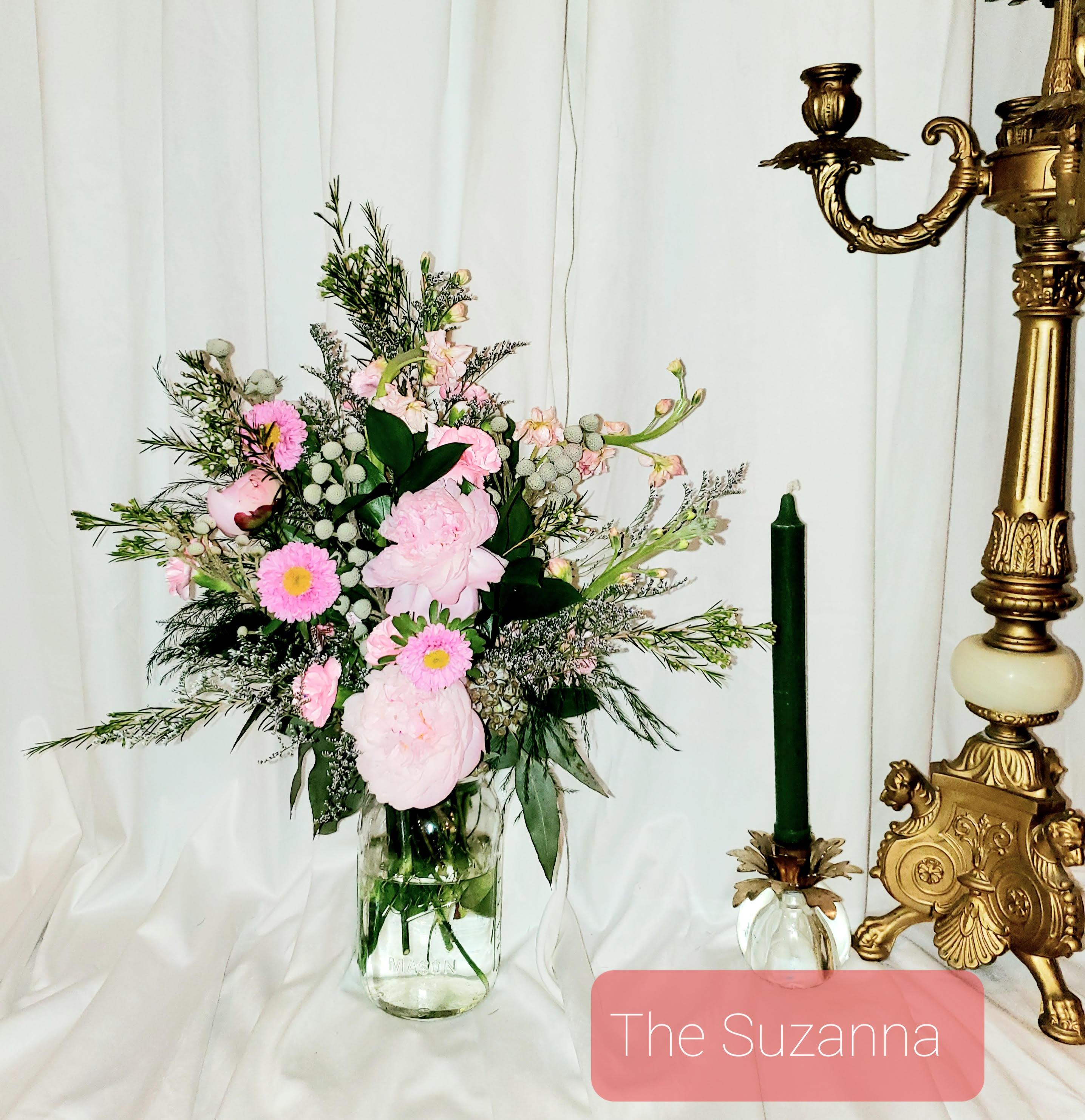 Pink floral arrangement in a clear glass vase beside a green candle holder