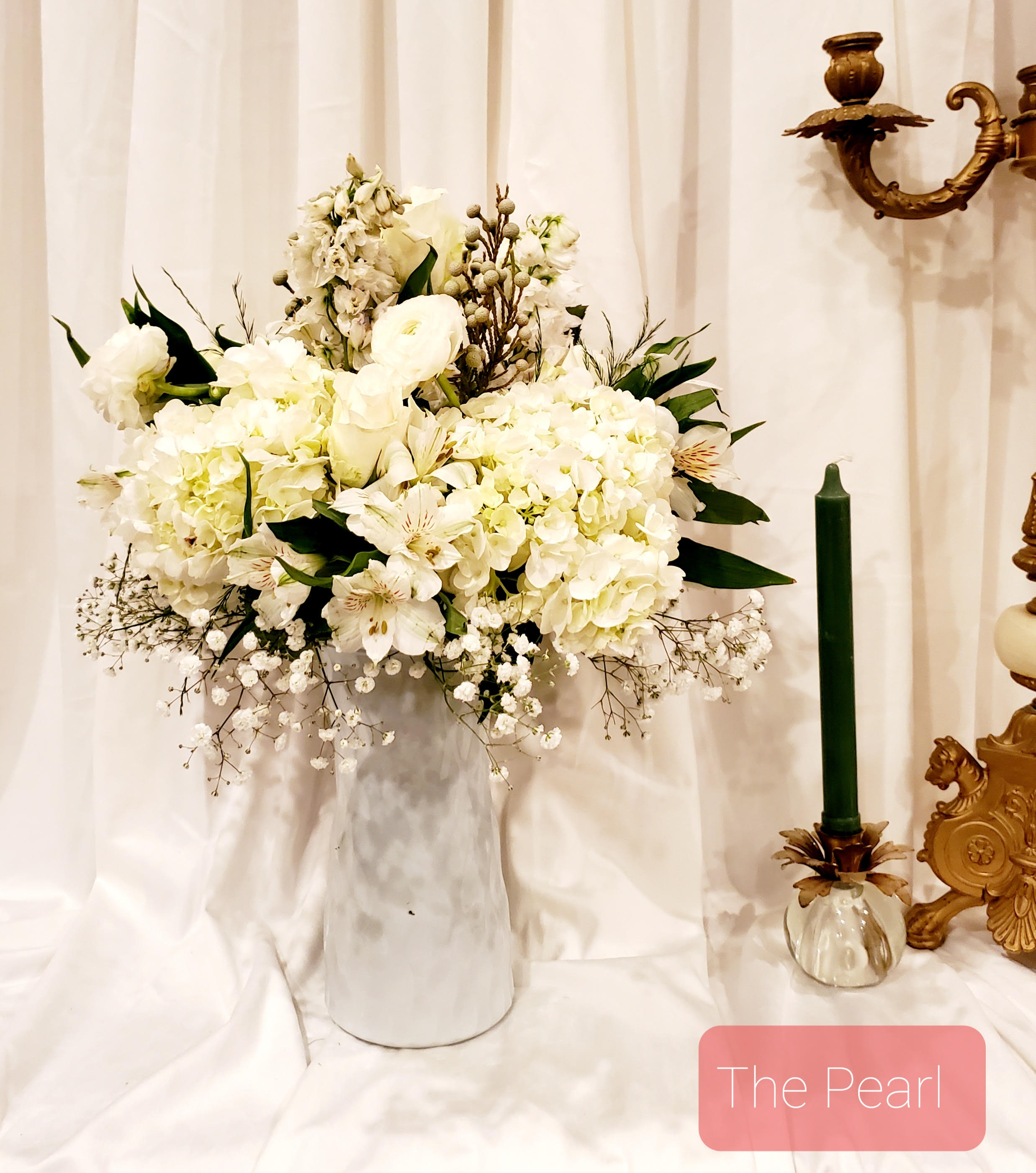 White floral arrangement in a tall vase beside a green candle