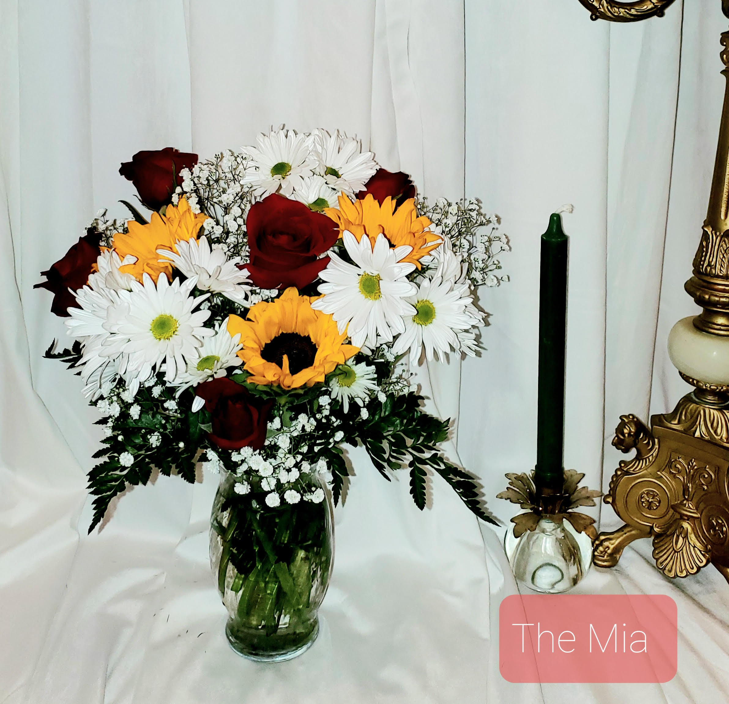 Bouquet of red roses, white daisies, and yellow sunflowers in a glass vase