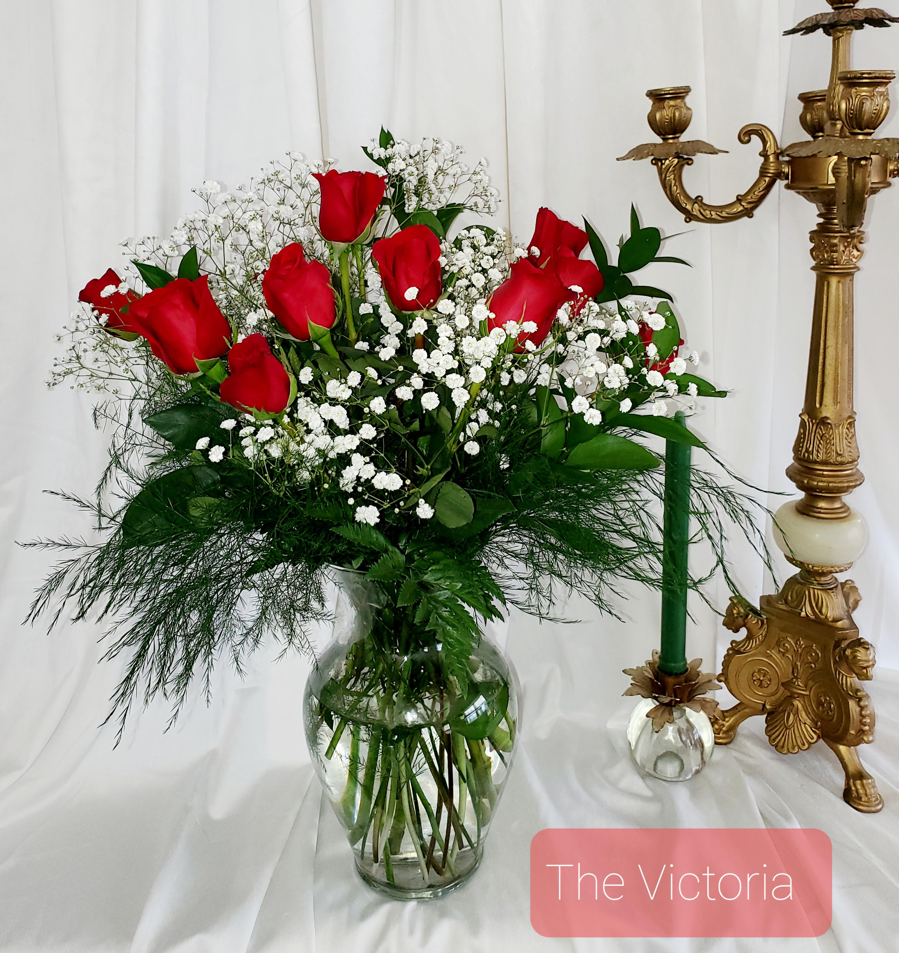 Red roses and baby's breath in a clear glass vase beside a gold candlestick