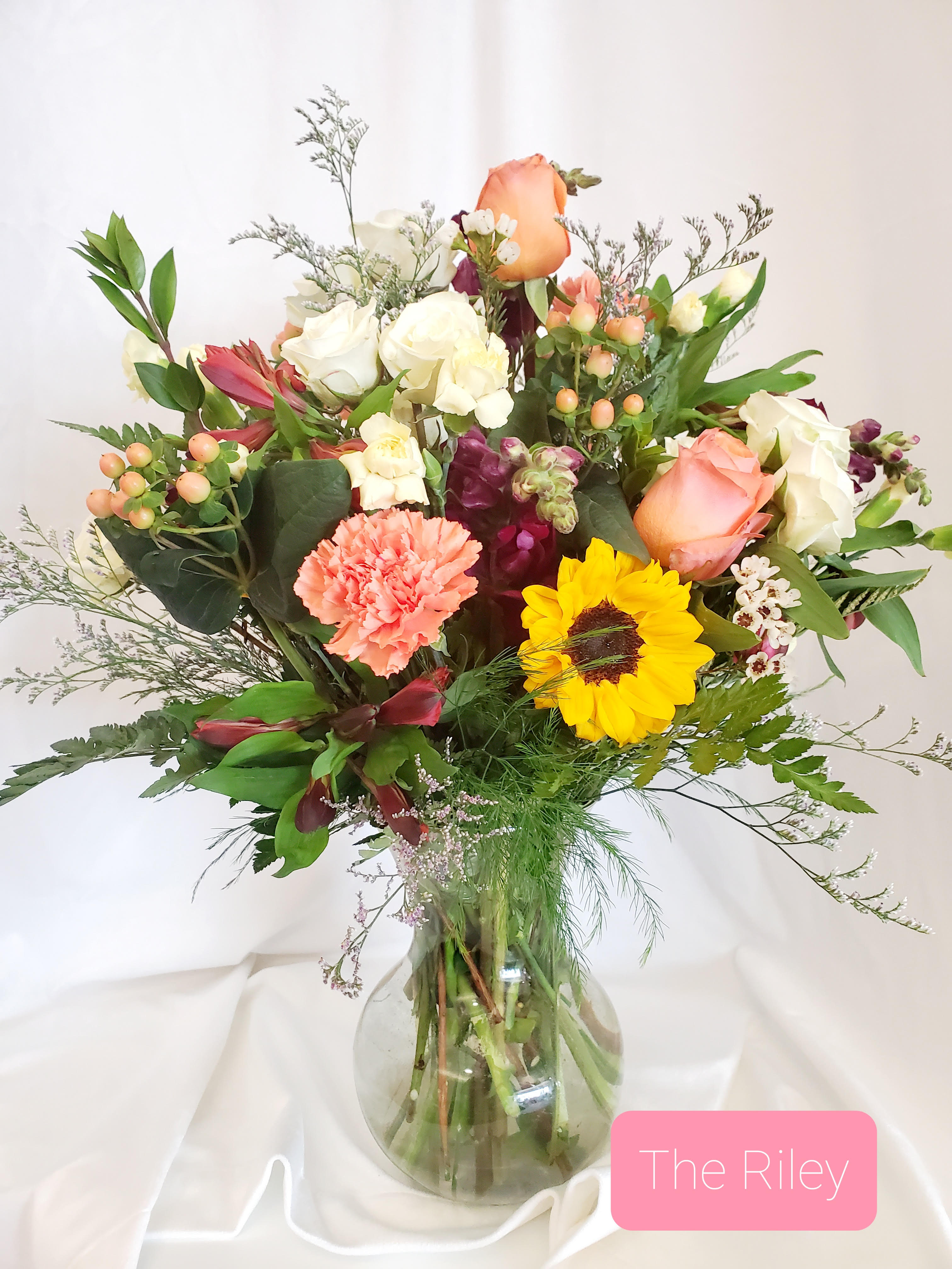 Mixed bouquet of roses, sunflower, and carnations in a glass vase