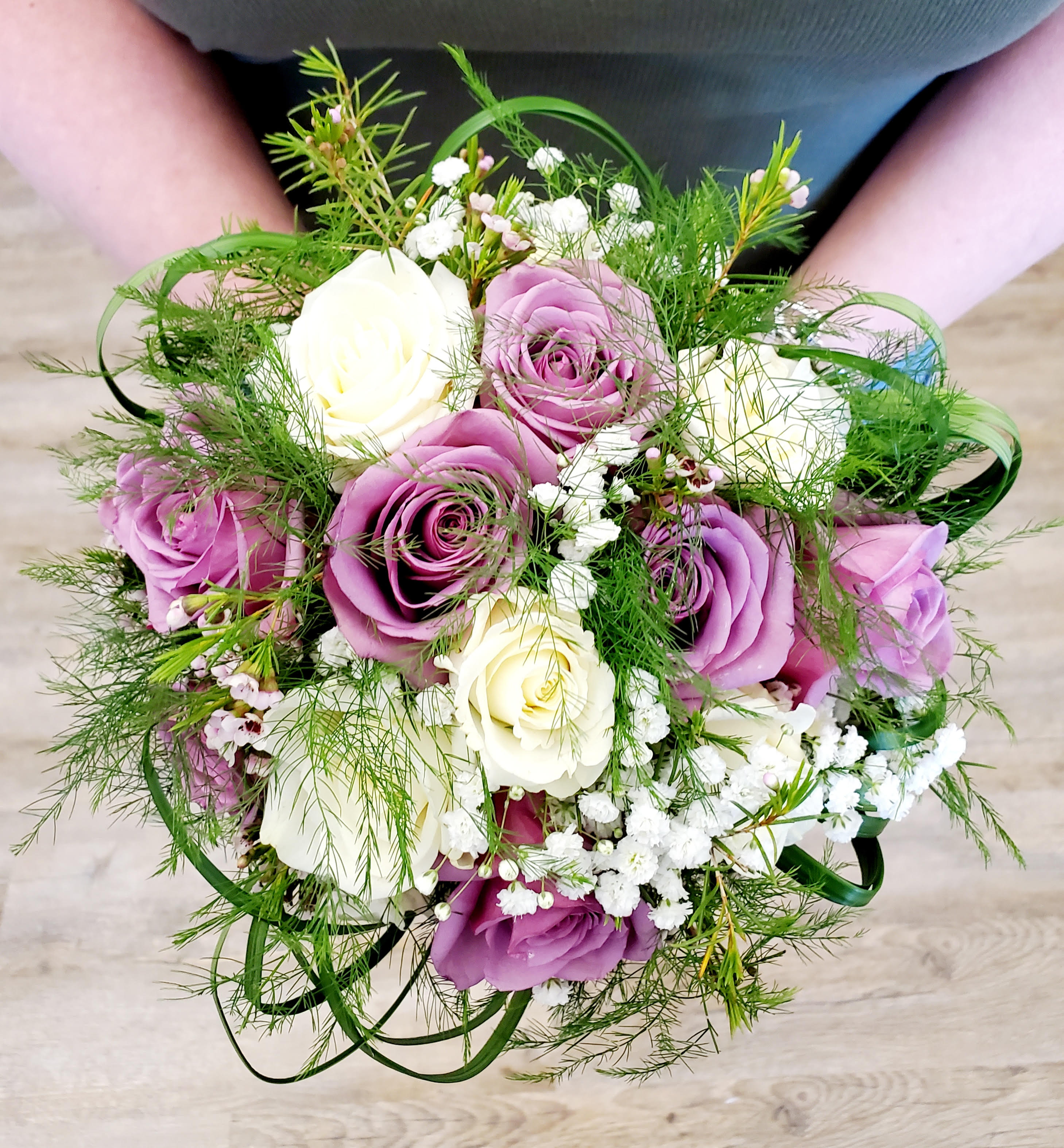 Handheld bouquet of purple and white roses with airy filler flowers
