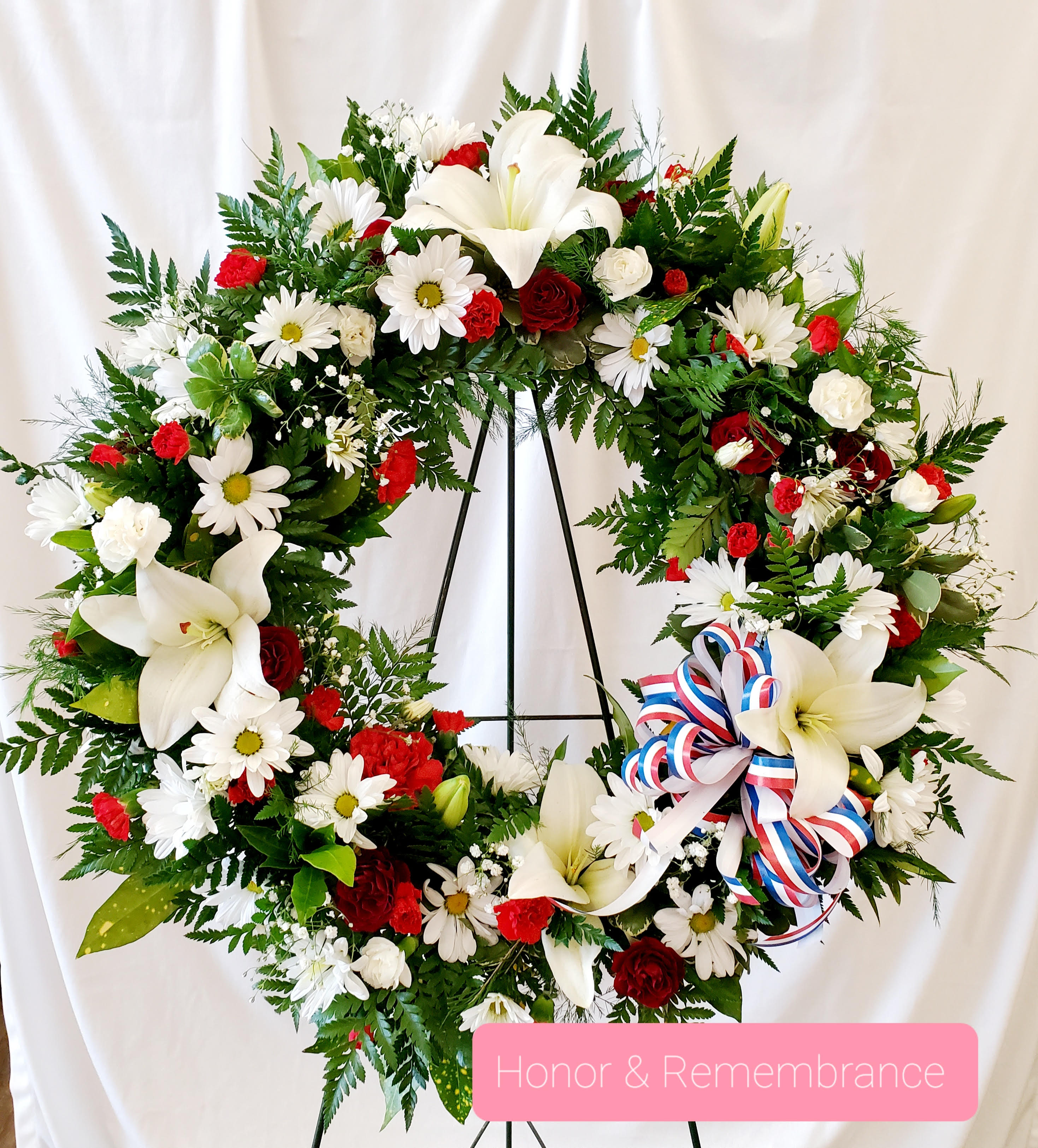 Large floral wreath with white lilies, daisies, and red roses on a stand