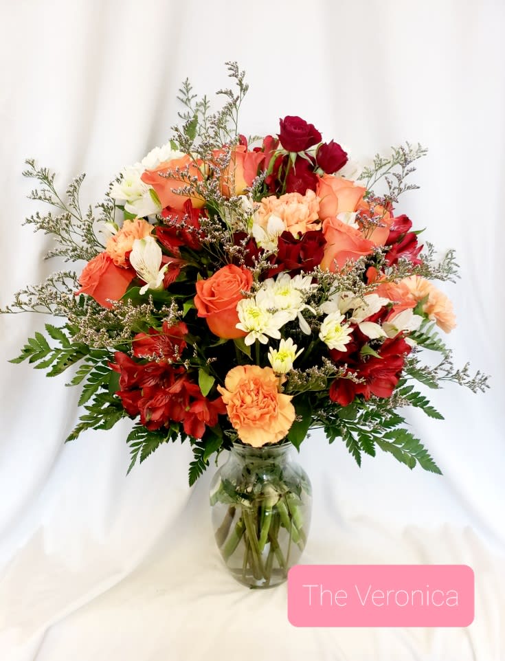 Mixed bouquet of red, peach, and white flowers in a glass vase