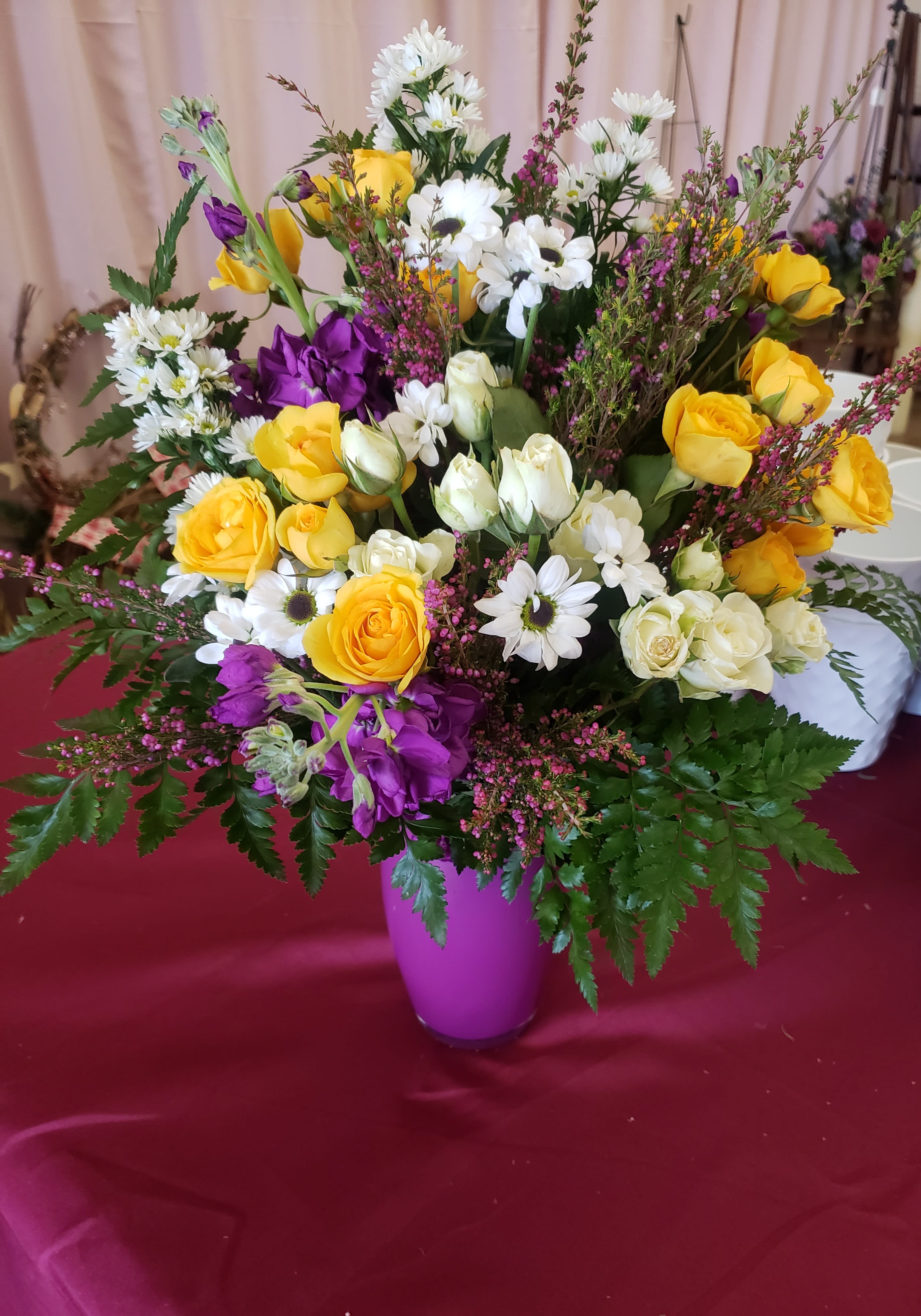 Mixed bouquet of yellow roses, white daisies, and purple flowers in a vase