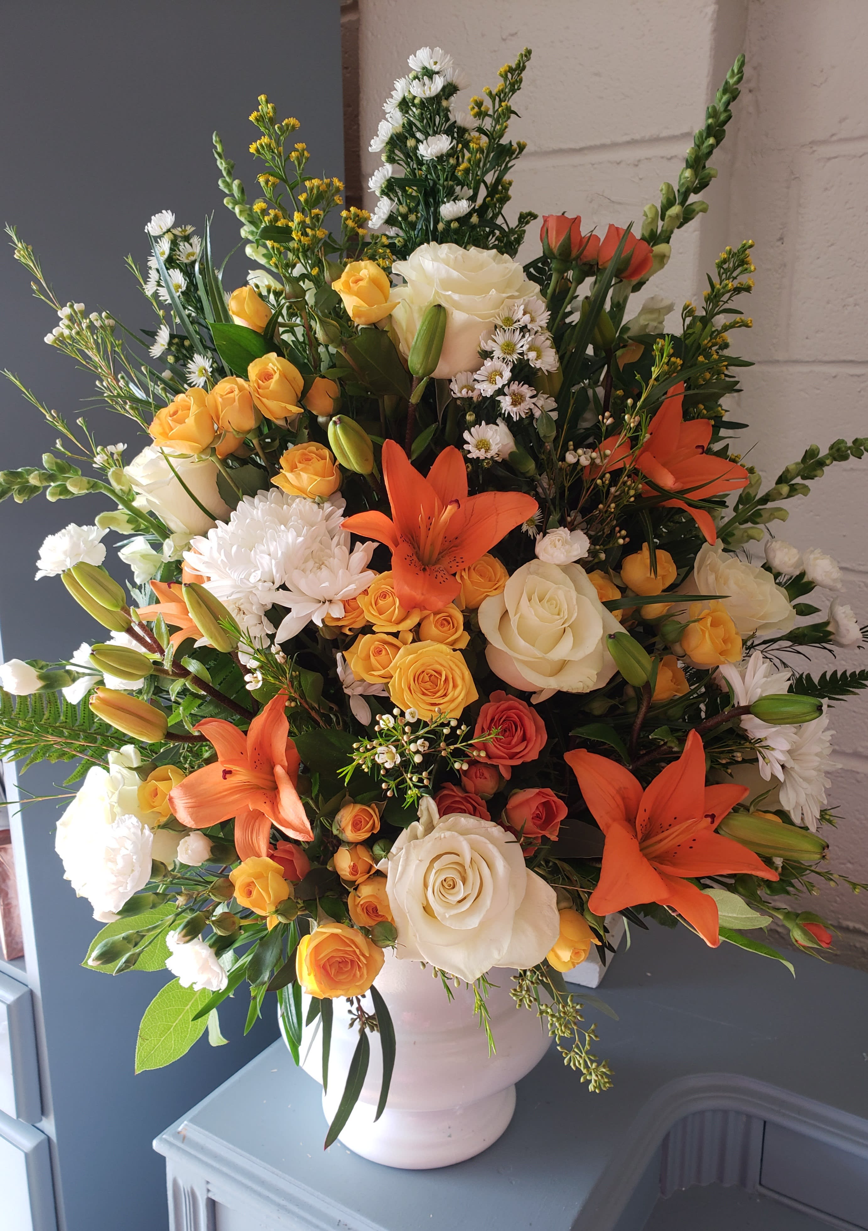 Large bouquet of orange lilies, white roses, and yellow spray roses in a white vase