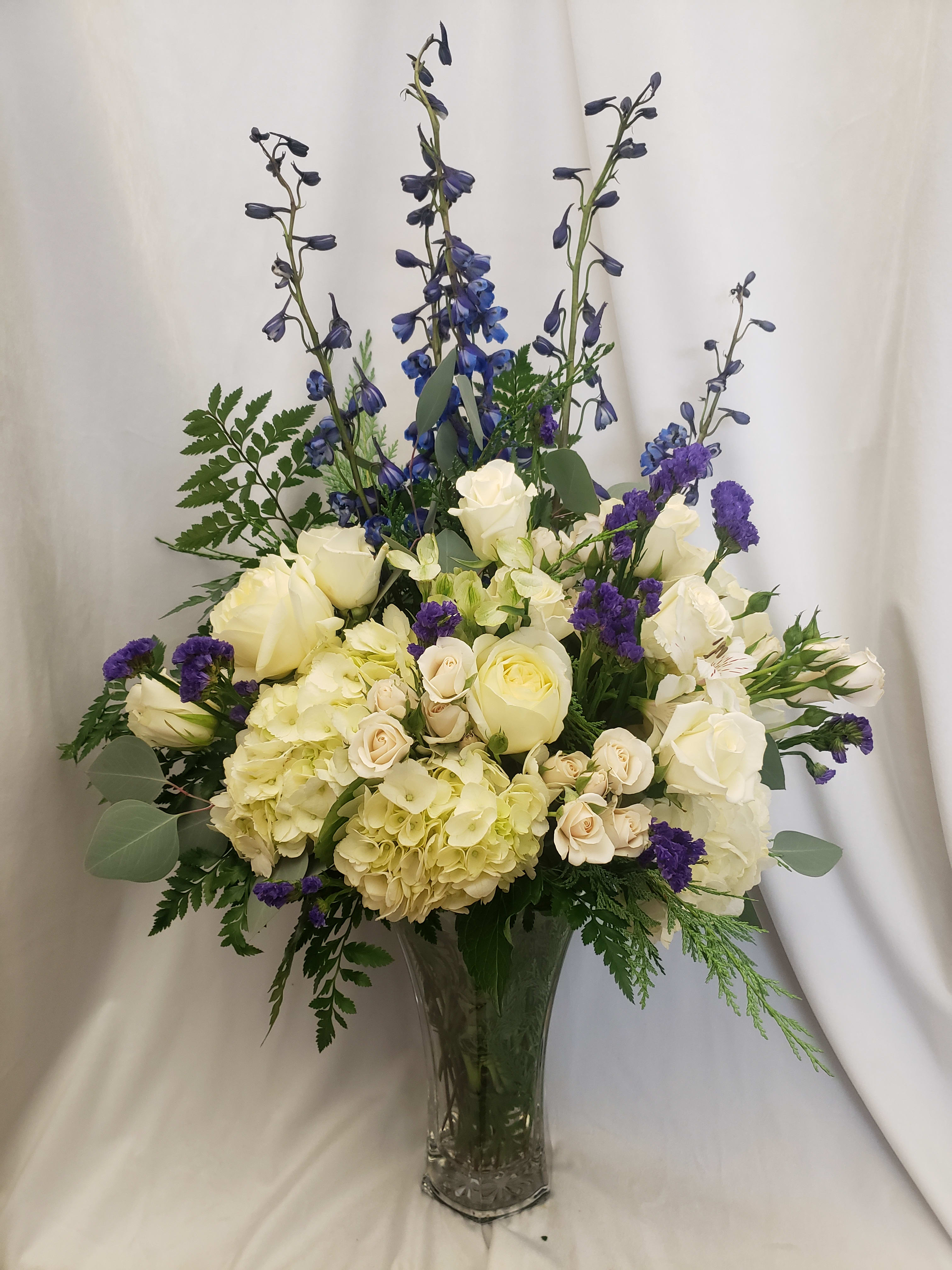 Tall bouquet of white roses, hydrangeas, and blue delphinium in a glass vase