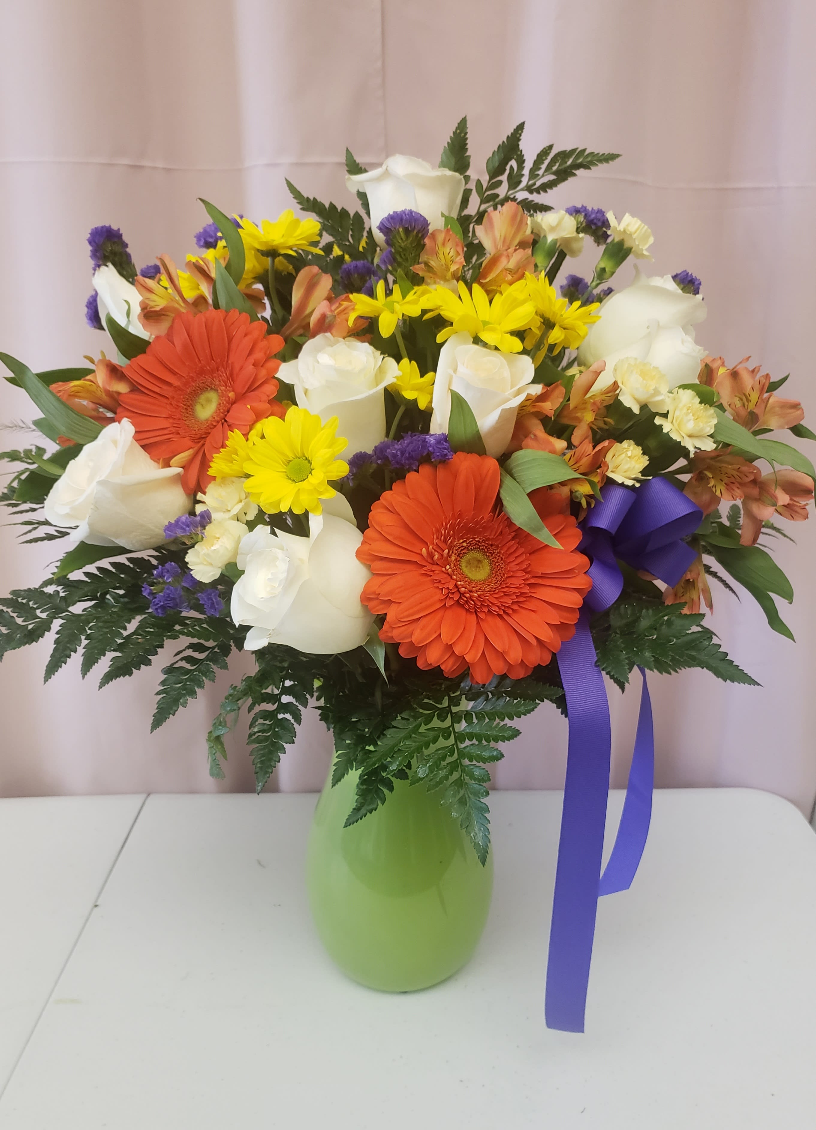 Mixed bouquet of white roses, orange gerberas, and yellow daisies in a green vase