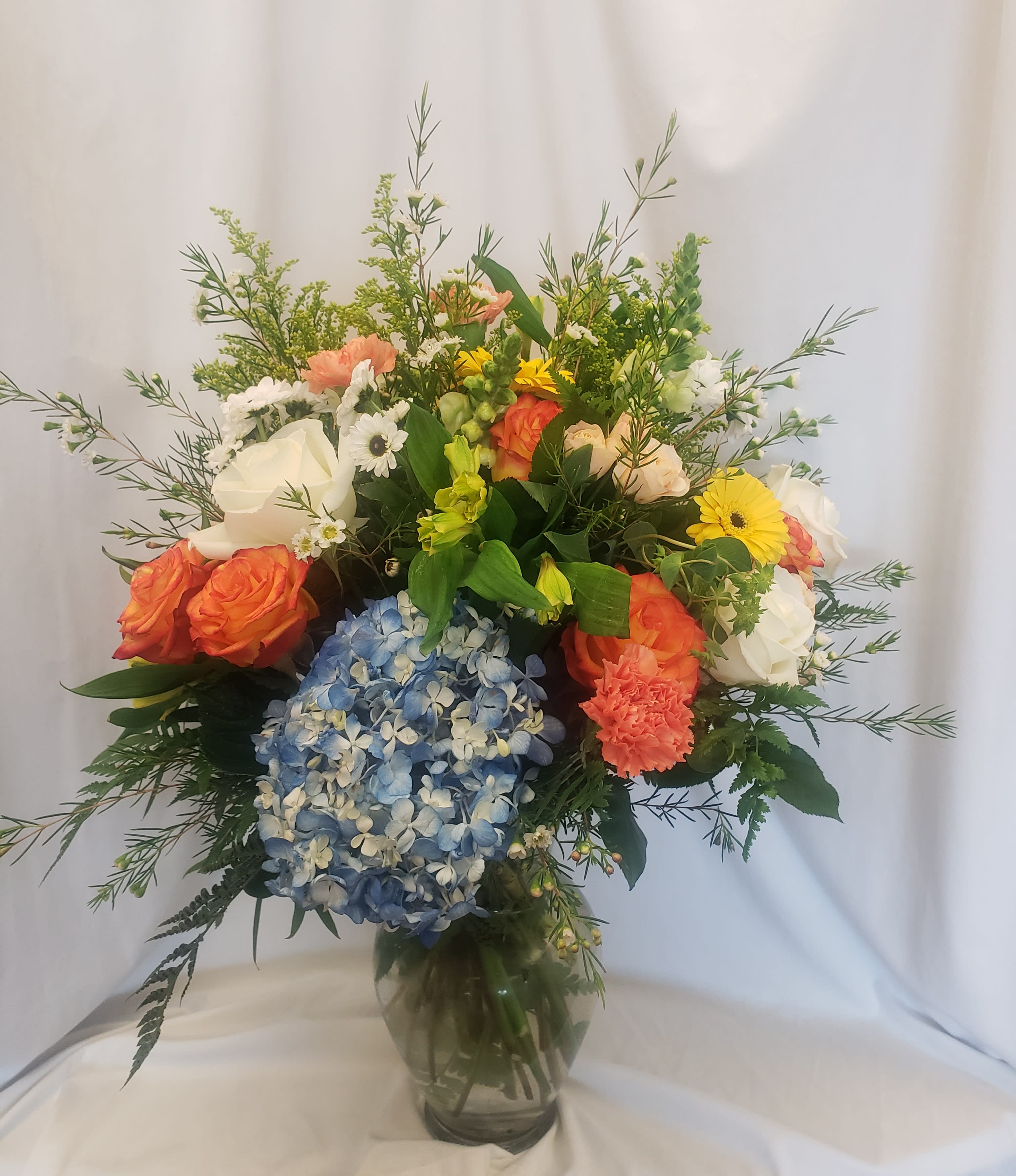 Mixed bouquet with hydrangea, roses, carnations, and daisies in a glass vase