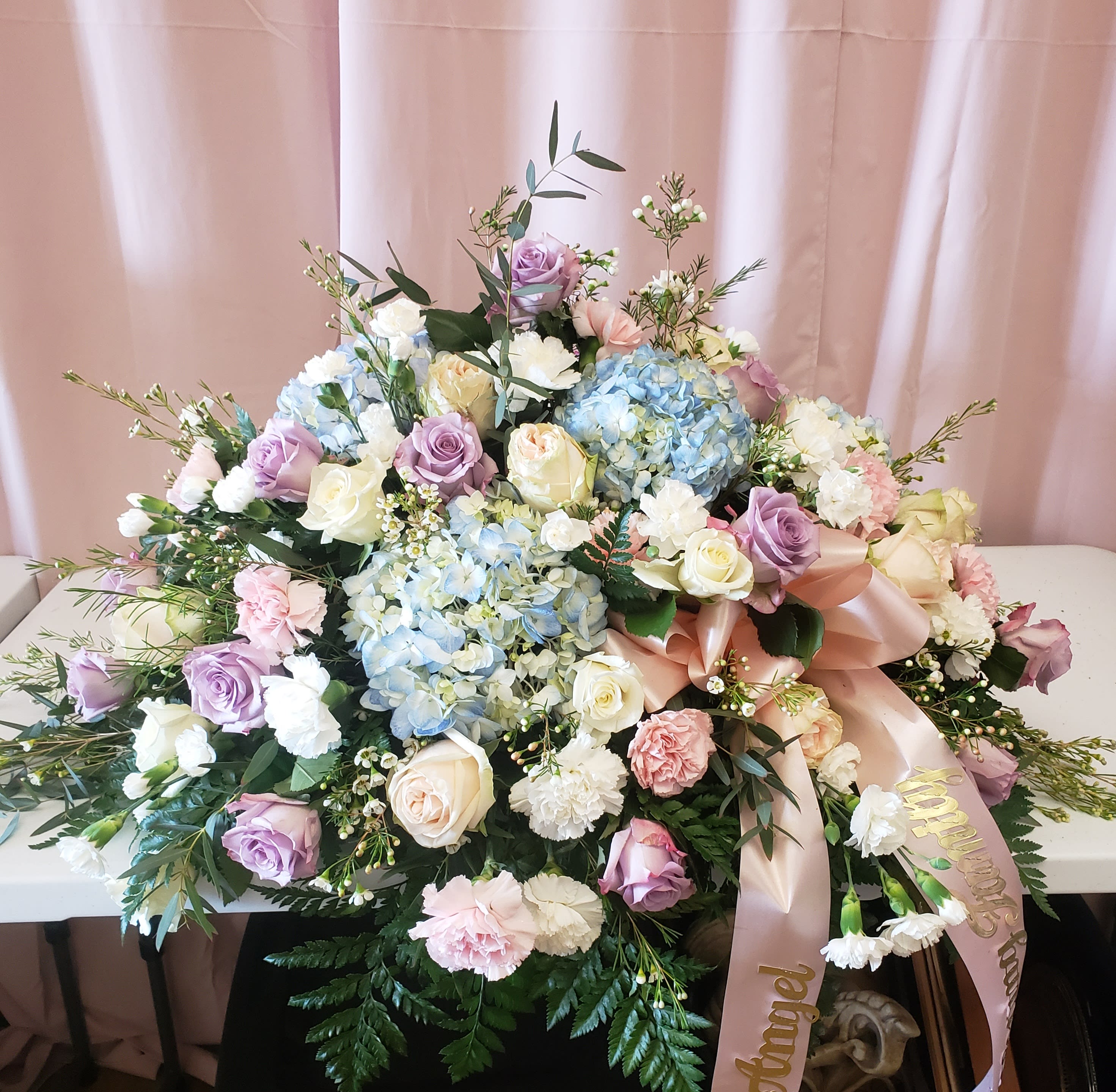 Large pastel floral arrangement with roses, hydrangeas, and carnations on a table