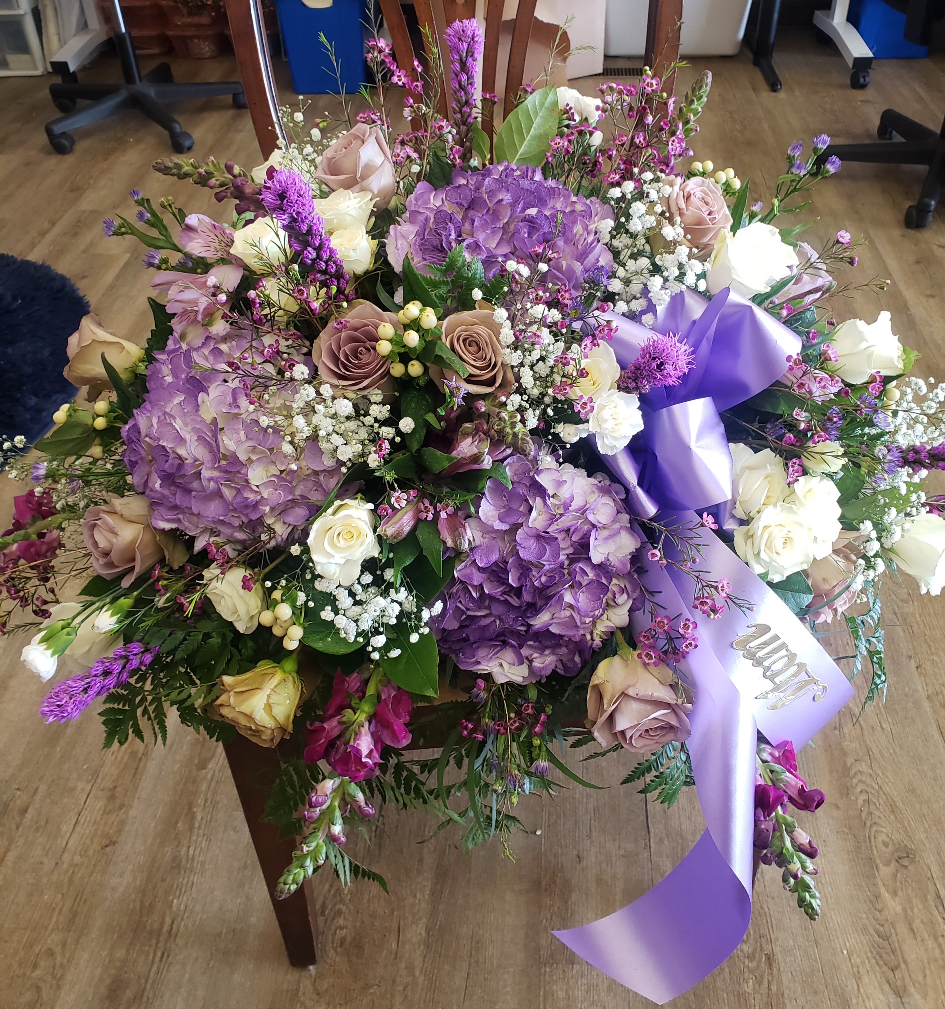 Large bouquet of purple hydrangeas, roses, and white flowers with a lavender ribbon