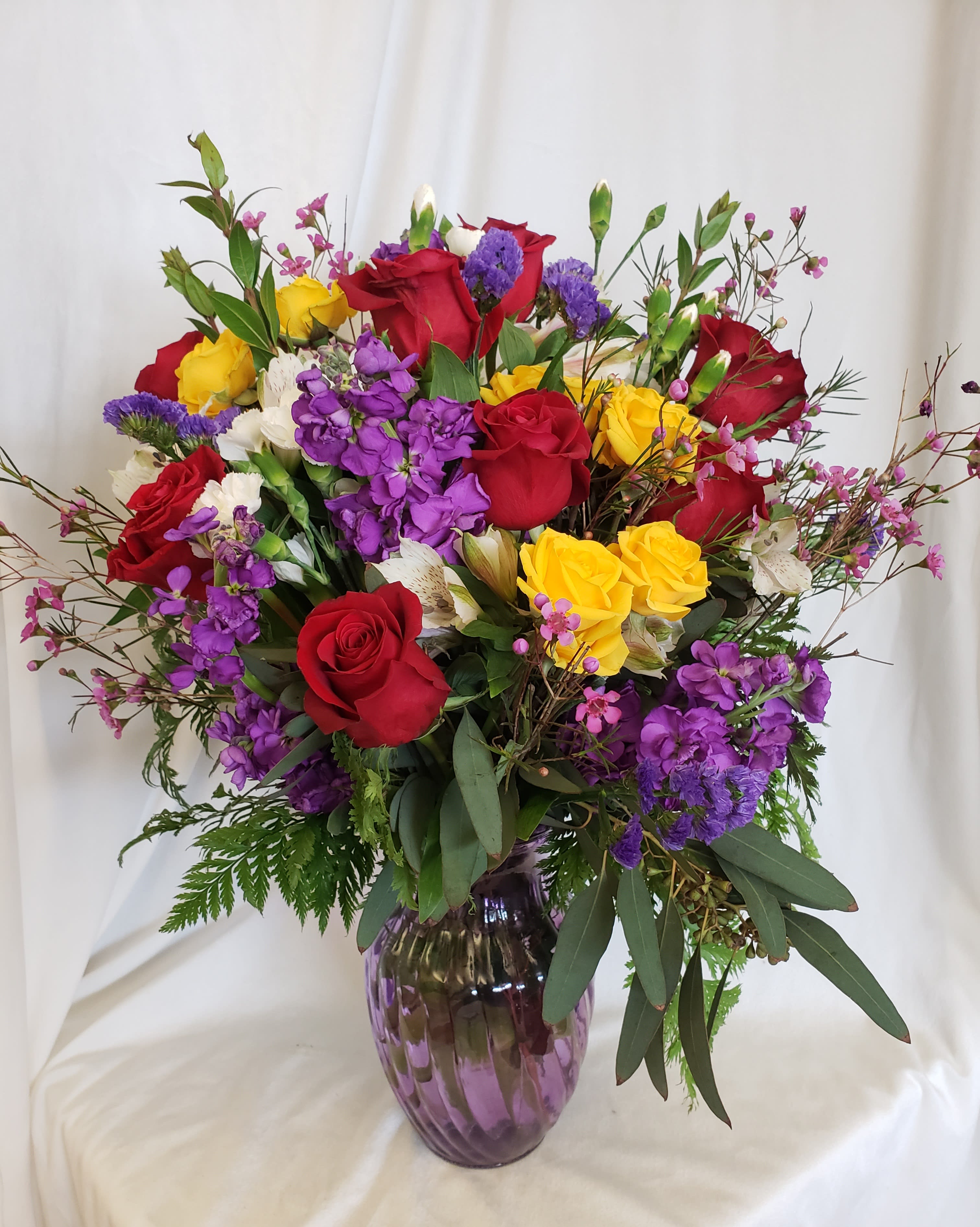 Mixed bouquet of red, yellow, and purple flowers in a purple glass vase