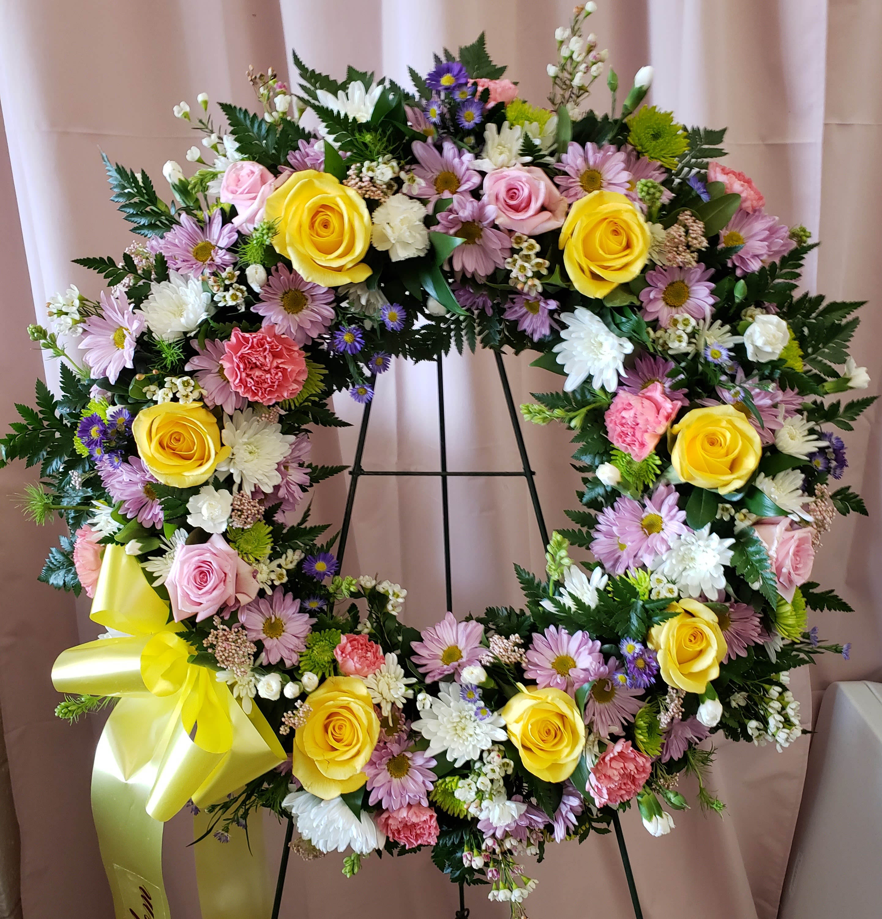 Large floral wreath with yellow roses, pink flowers, and a yellow ribbon