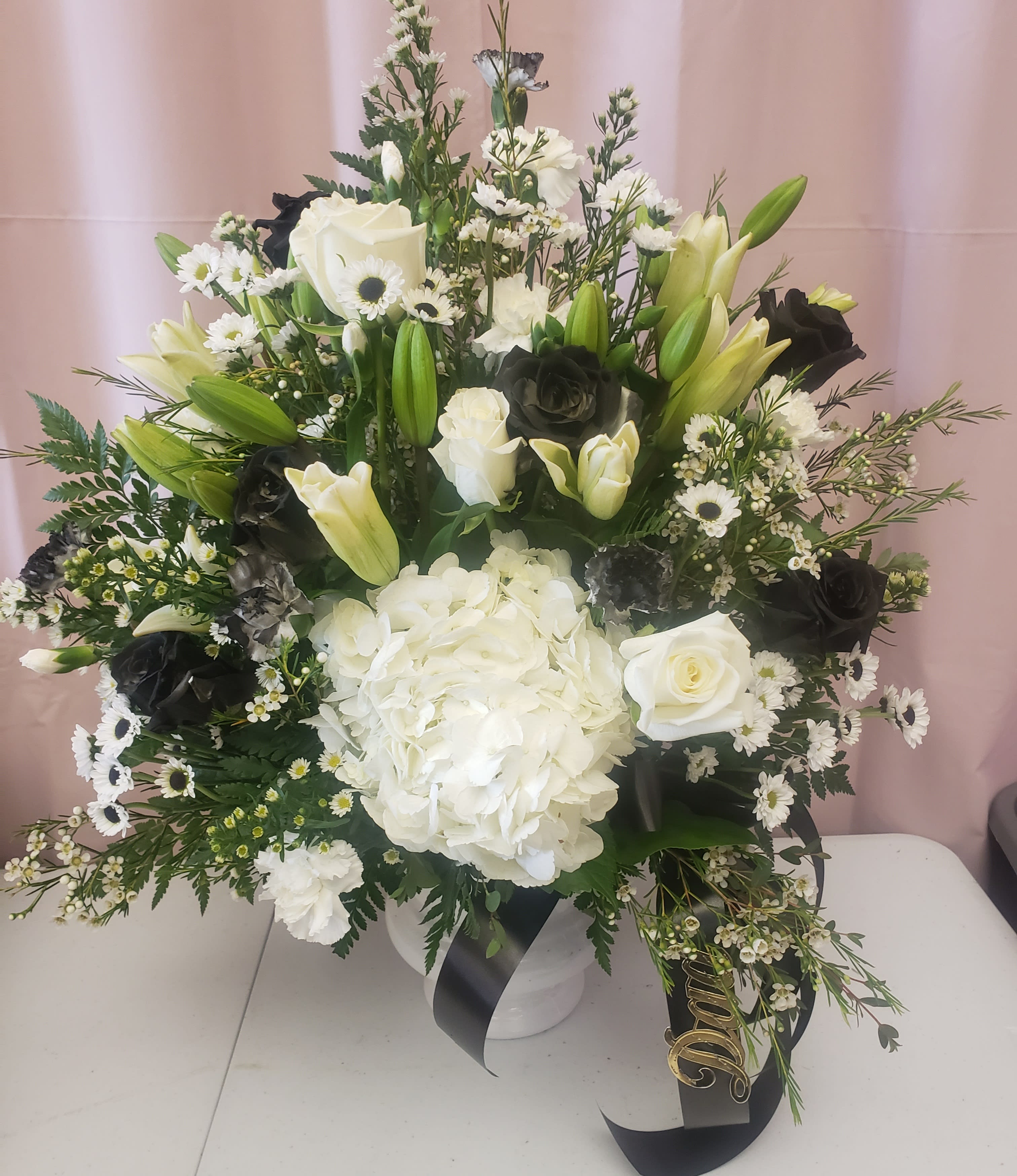 White and black floral arrangement in a white vase with lilies, roses, and hydrangea