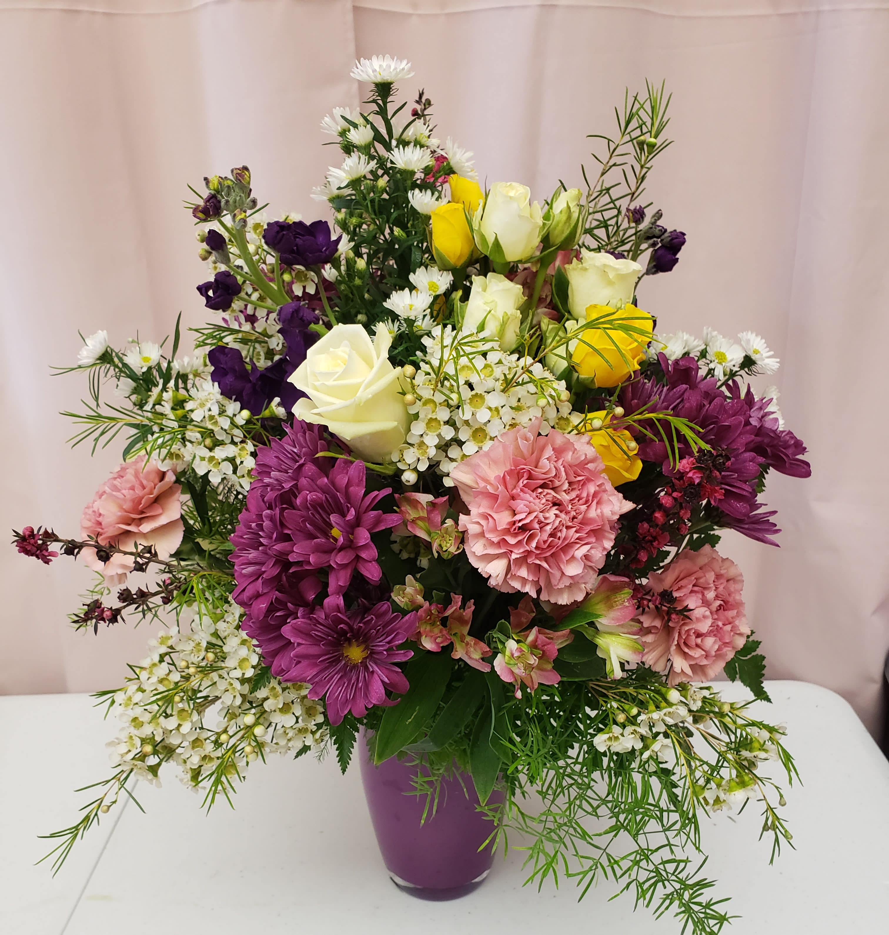 Mixed bouquet in a purple vase with roses, carnations, and purple daisies