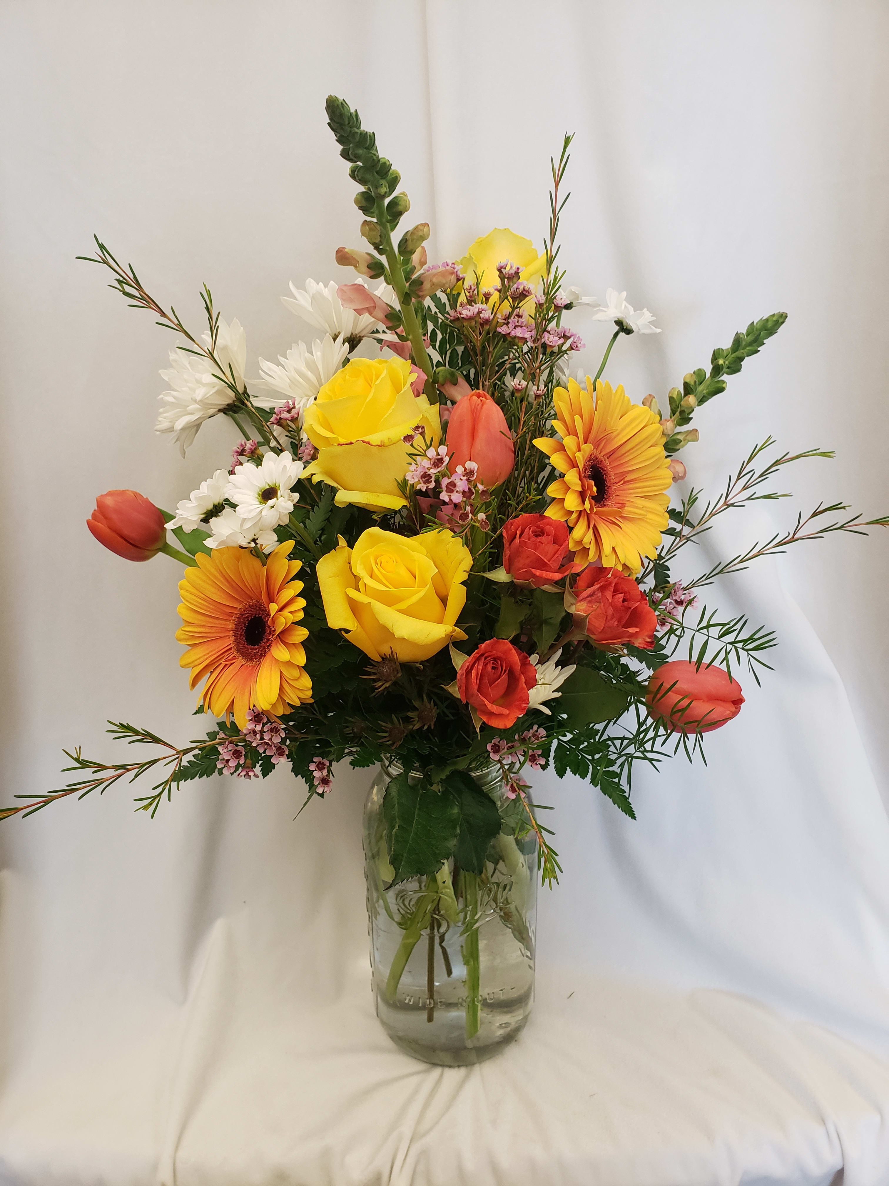 Mixed bouquet of yellow, orange, red, and white flowers in a glass vase