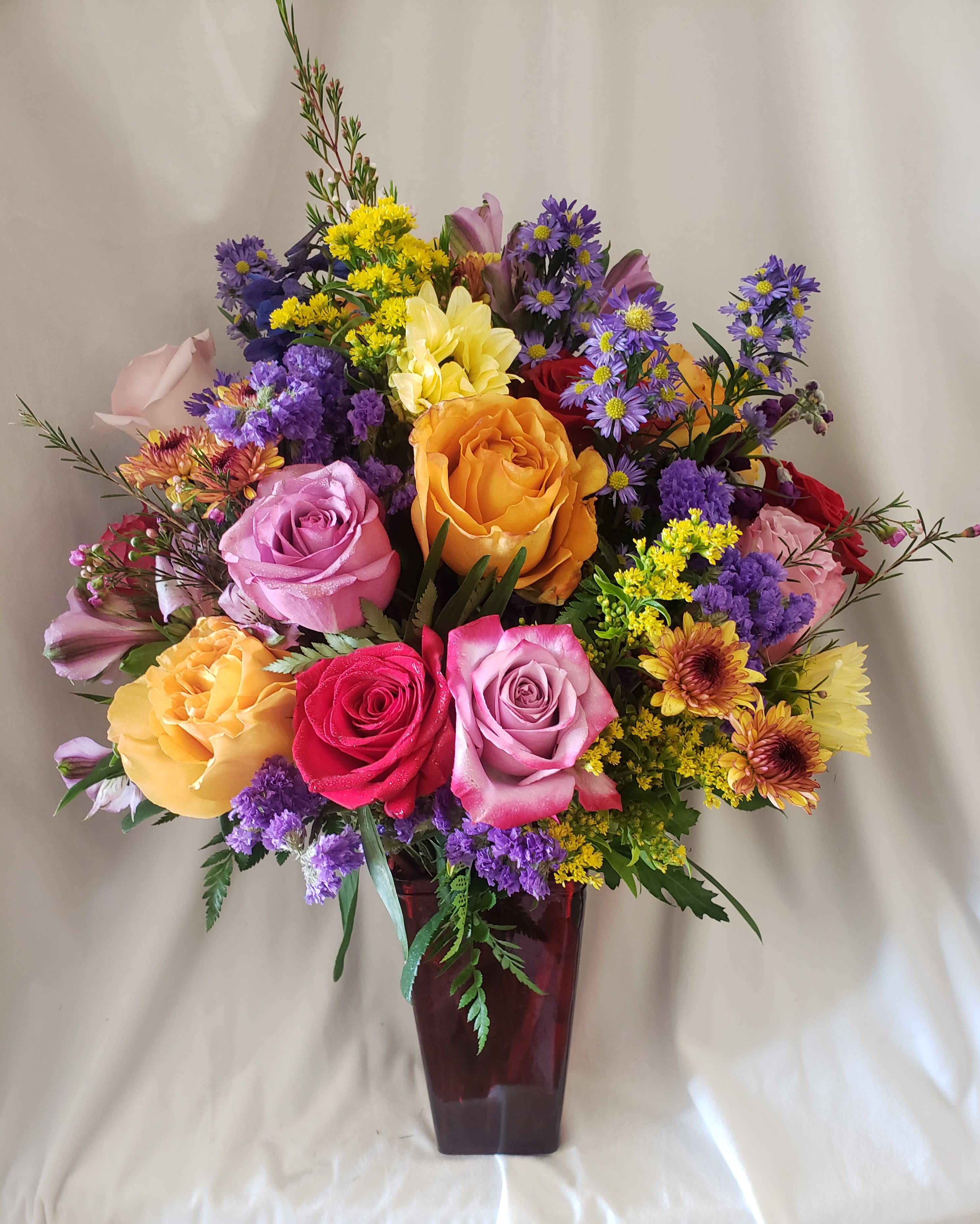 Mixed bouquet of roses and purple filler flowers in a burgundy vase