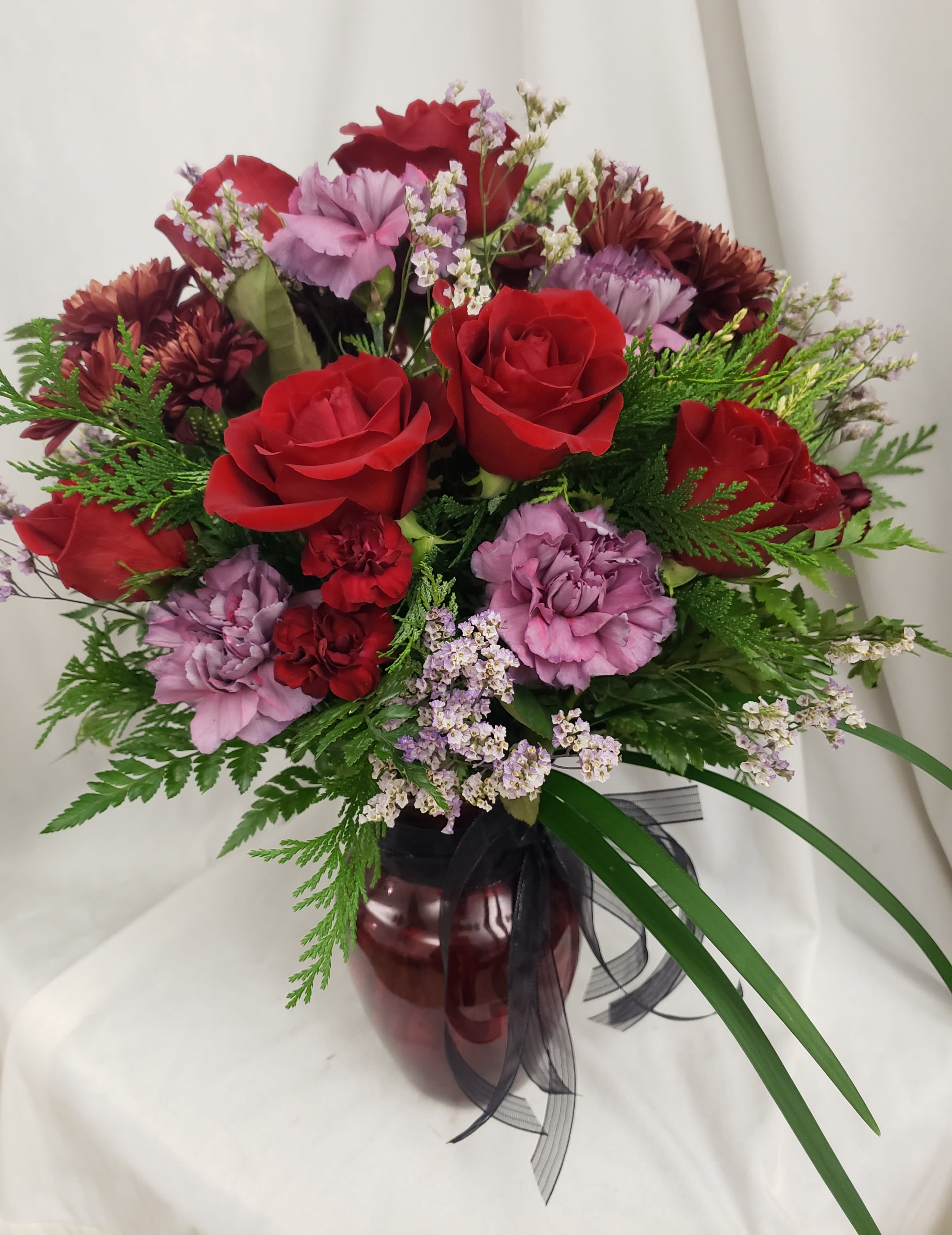Bouquet of red roses and purple carnations in a burgundy vase