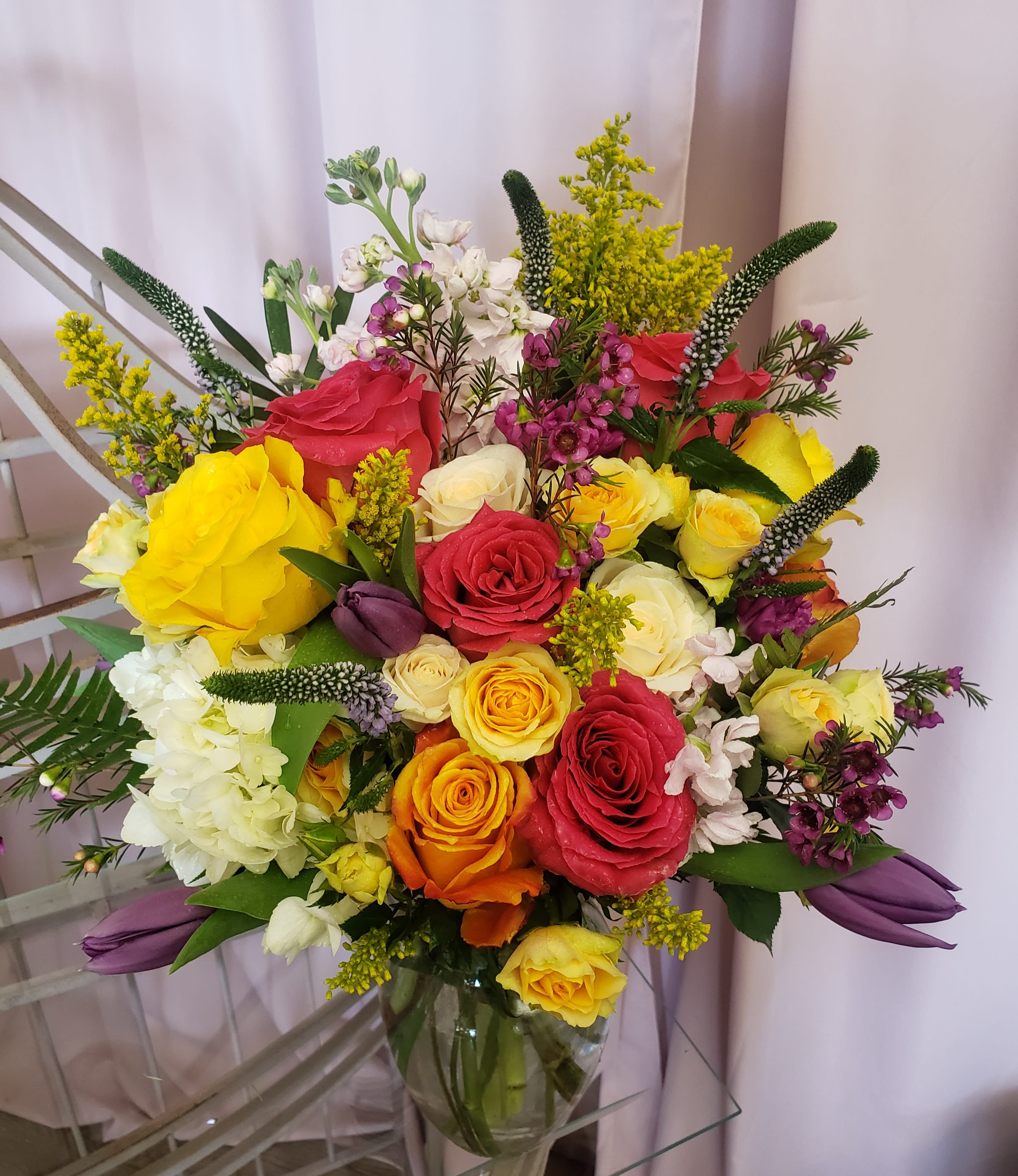 Mixed bouquet of roses, white blooms, and purple accents in a glass vase